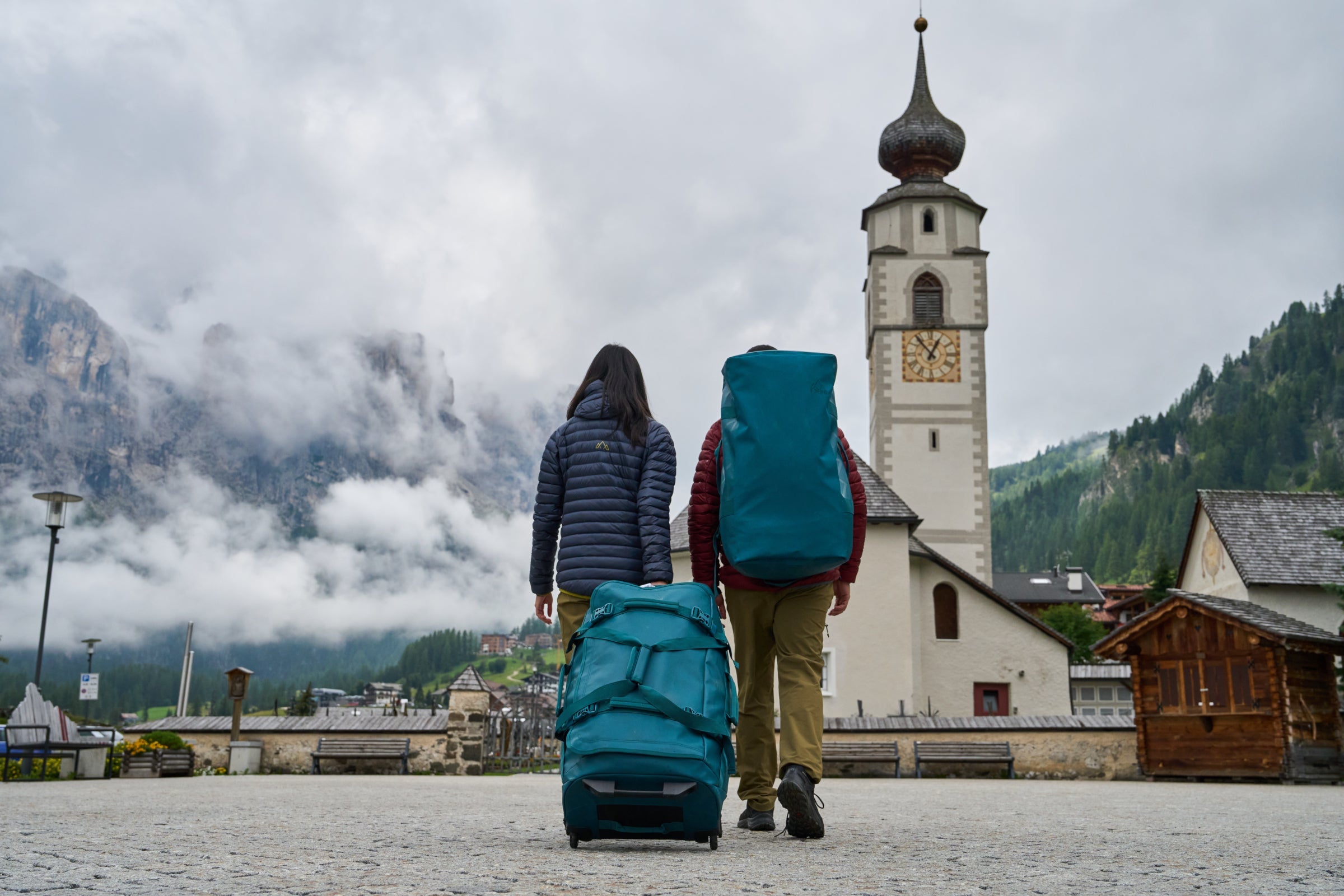 Fjern Luggage being carried through an Italian village in the Dolomites with cloudy mountains and a Church steeple in the distance