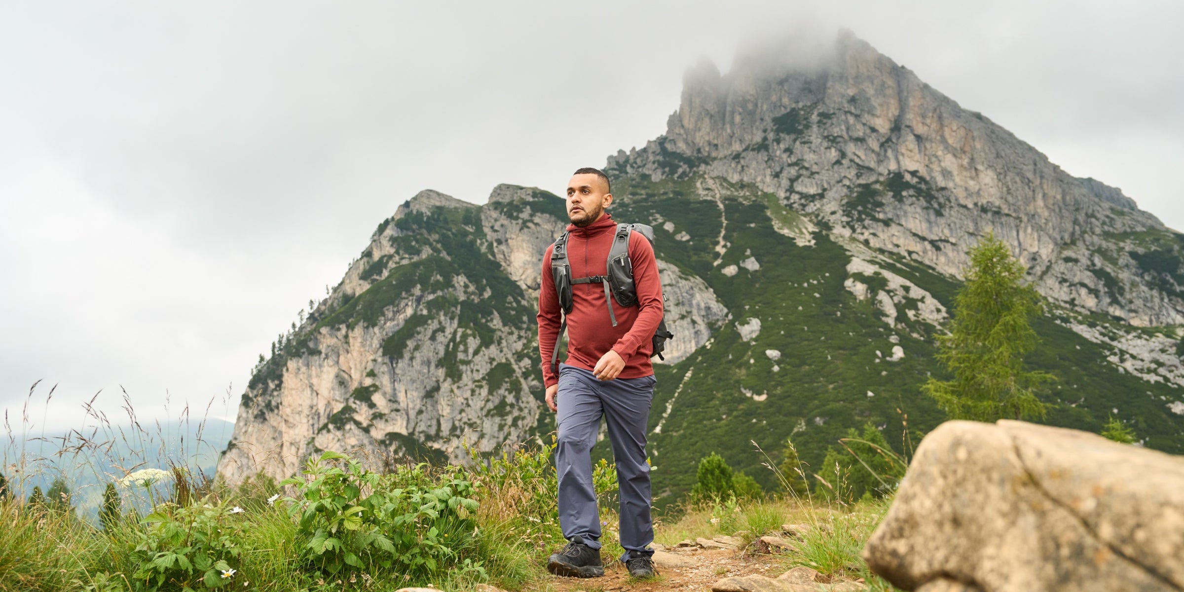 Man hiking on rocky mountain trail wearing Fjern long sleeve performance top.