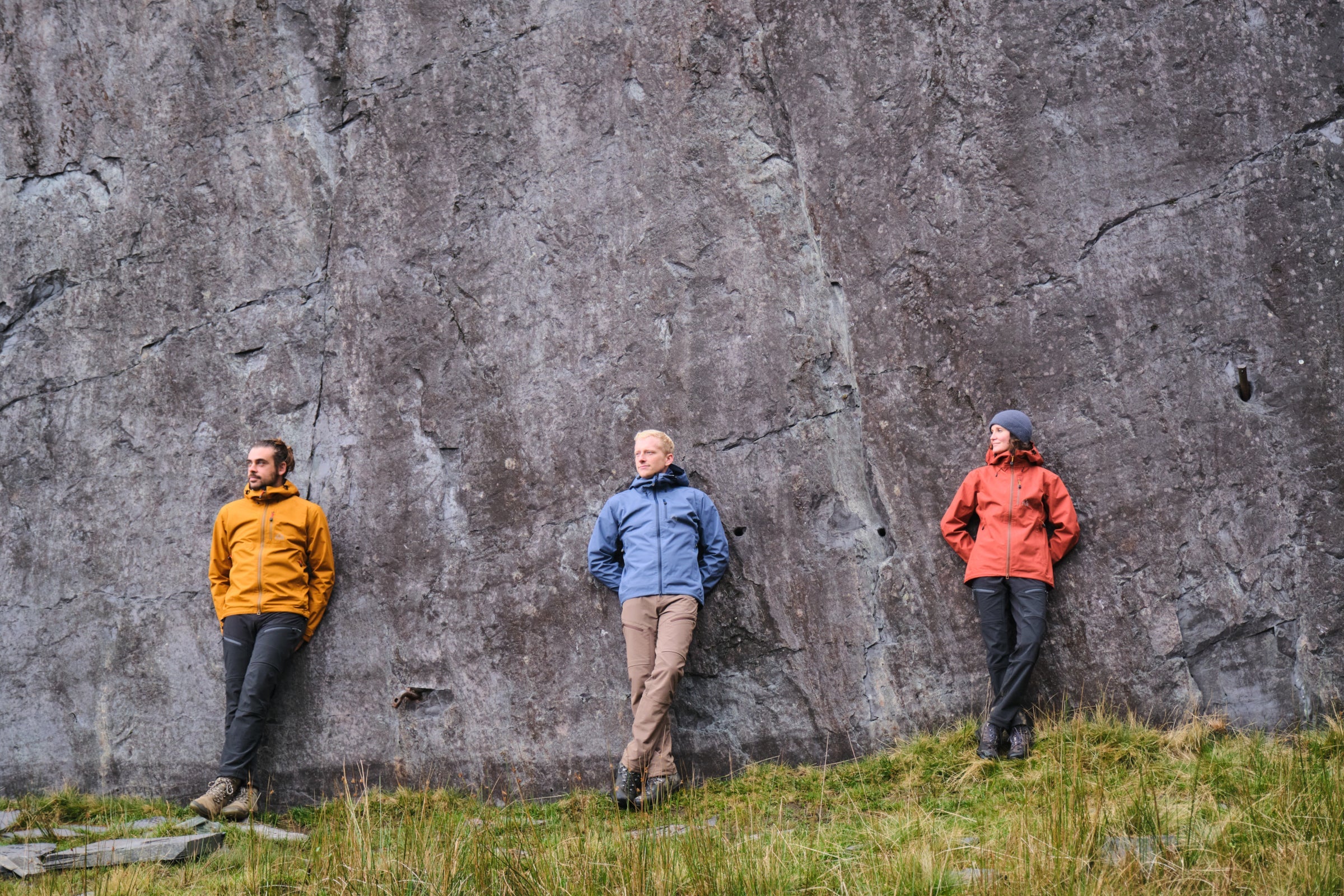 Three people wearing Fjern Forsvar jackets, standing against a large rock face