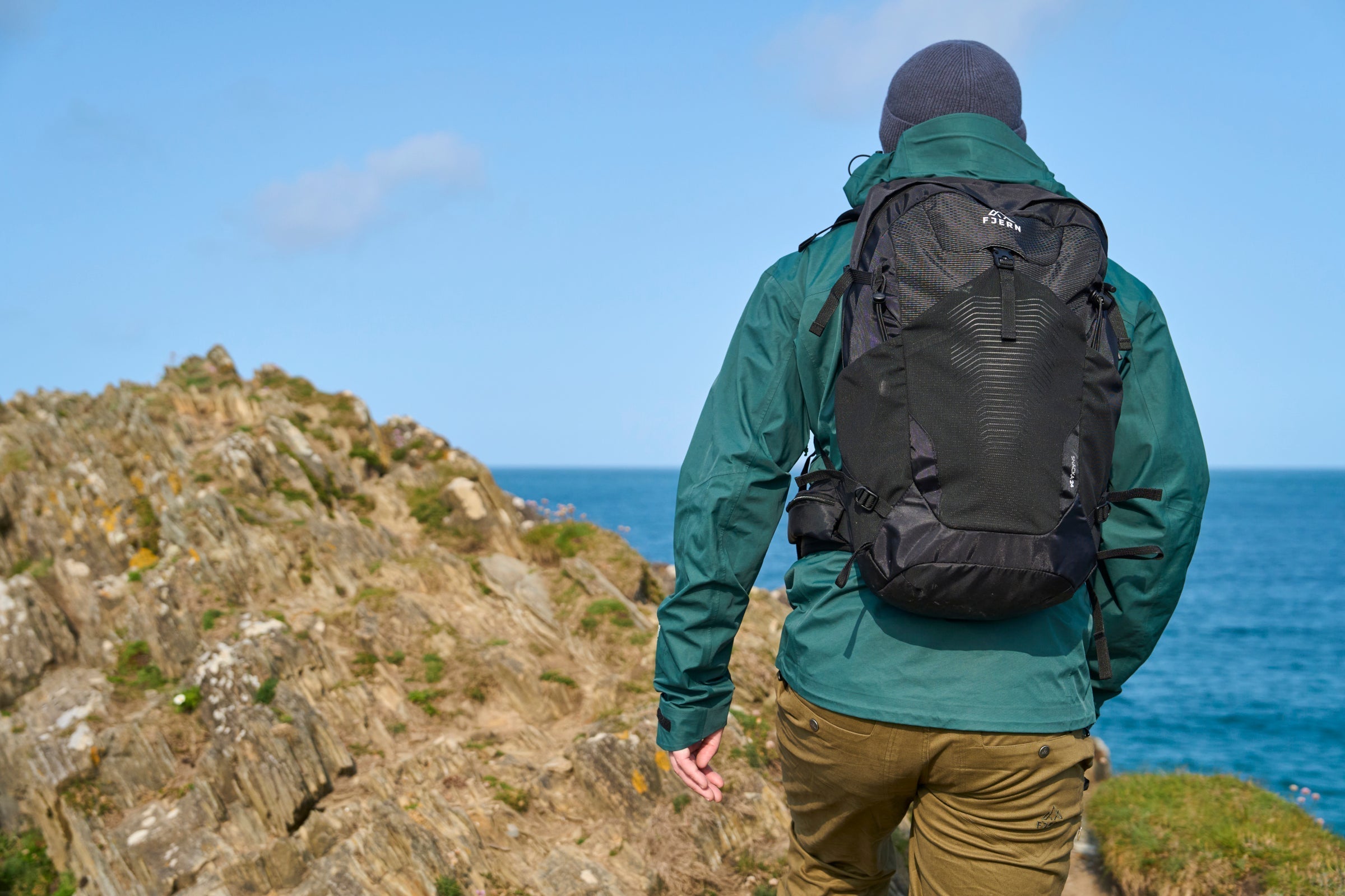 Hiker wearing a green jacket and backpack walking along a coastal trail