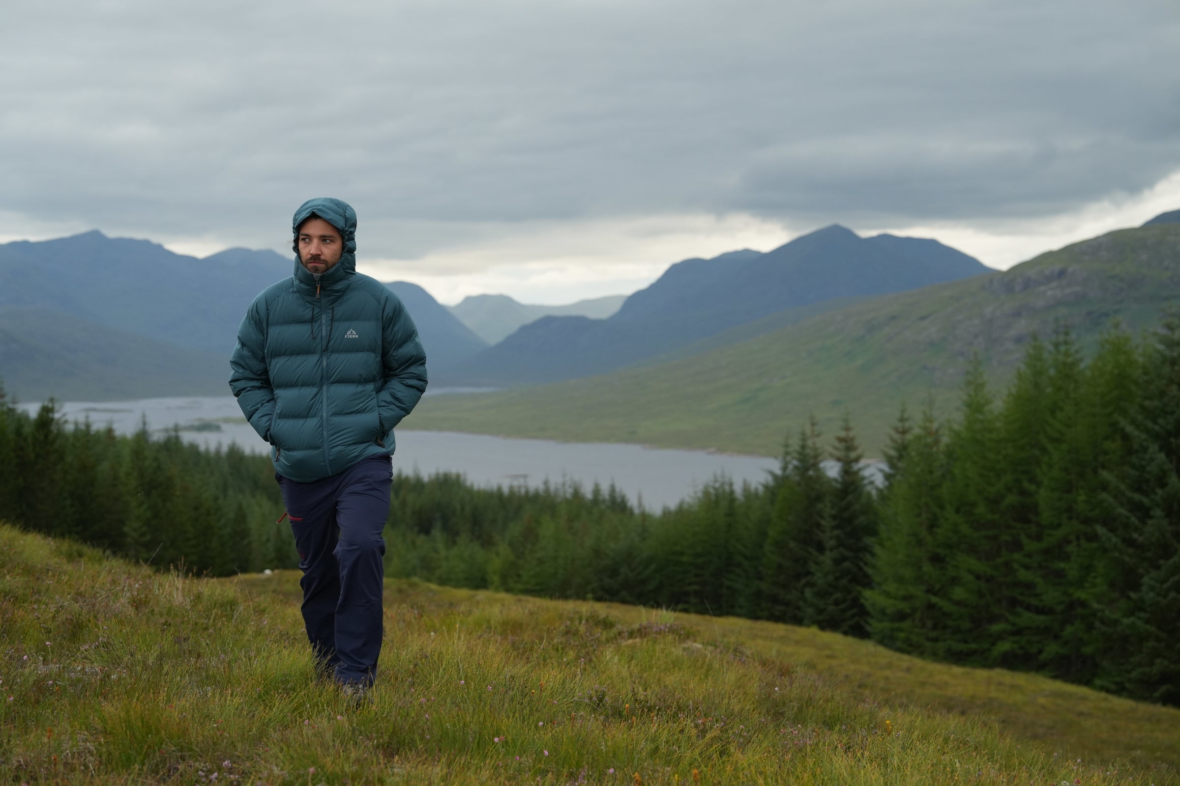 Man wearing a Fjern down jacket walking on a hillside in the mountains