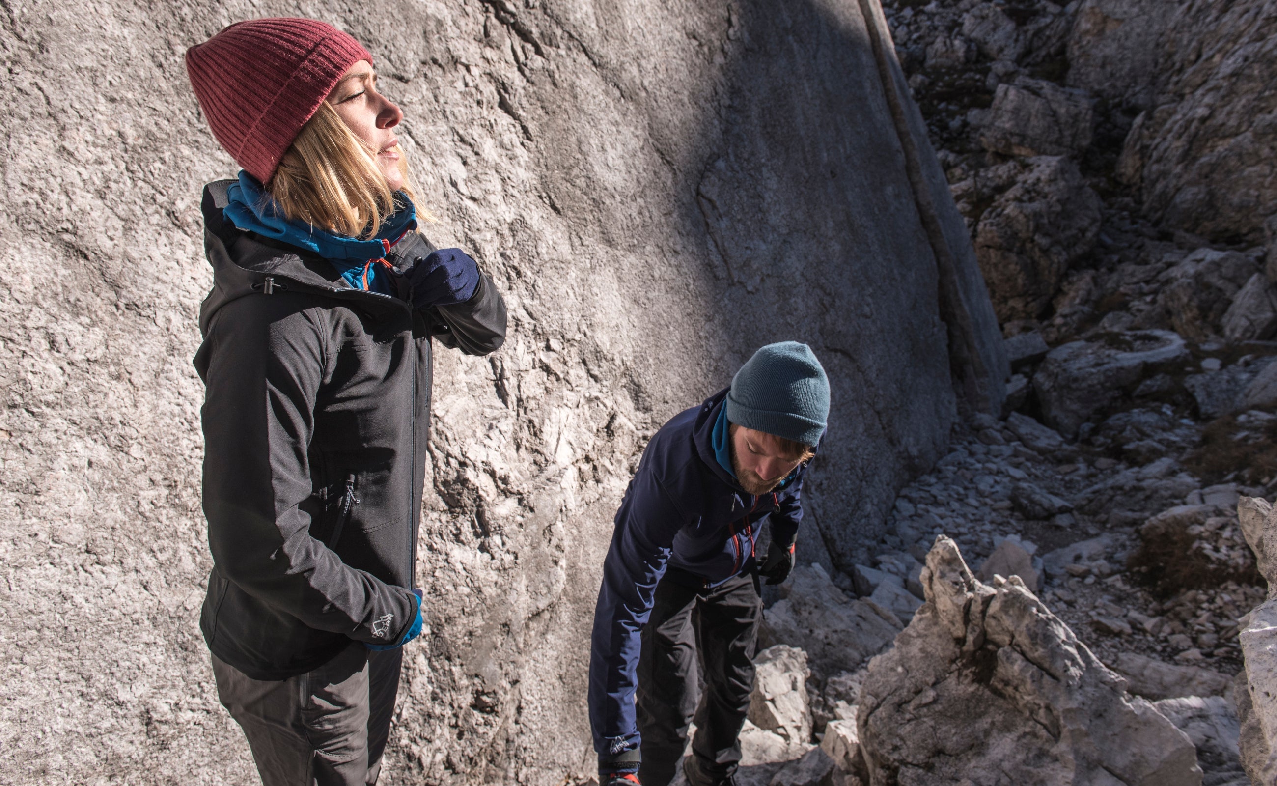 Two people climbing over rocky terrain wearing Fjern Grenser jackets