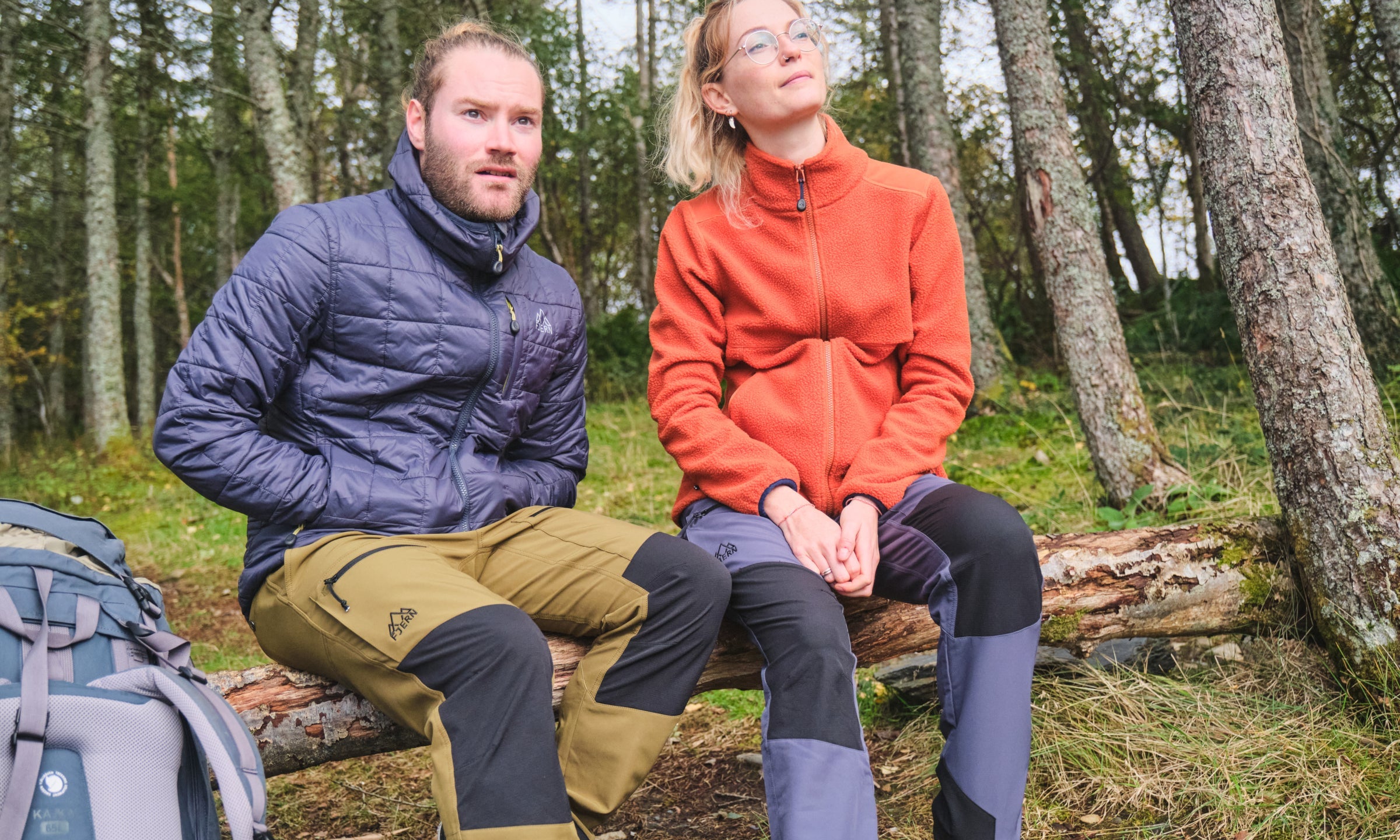 Two people in Fjern clothing seated on a log in a woodland area