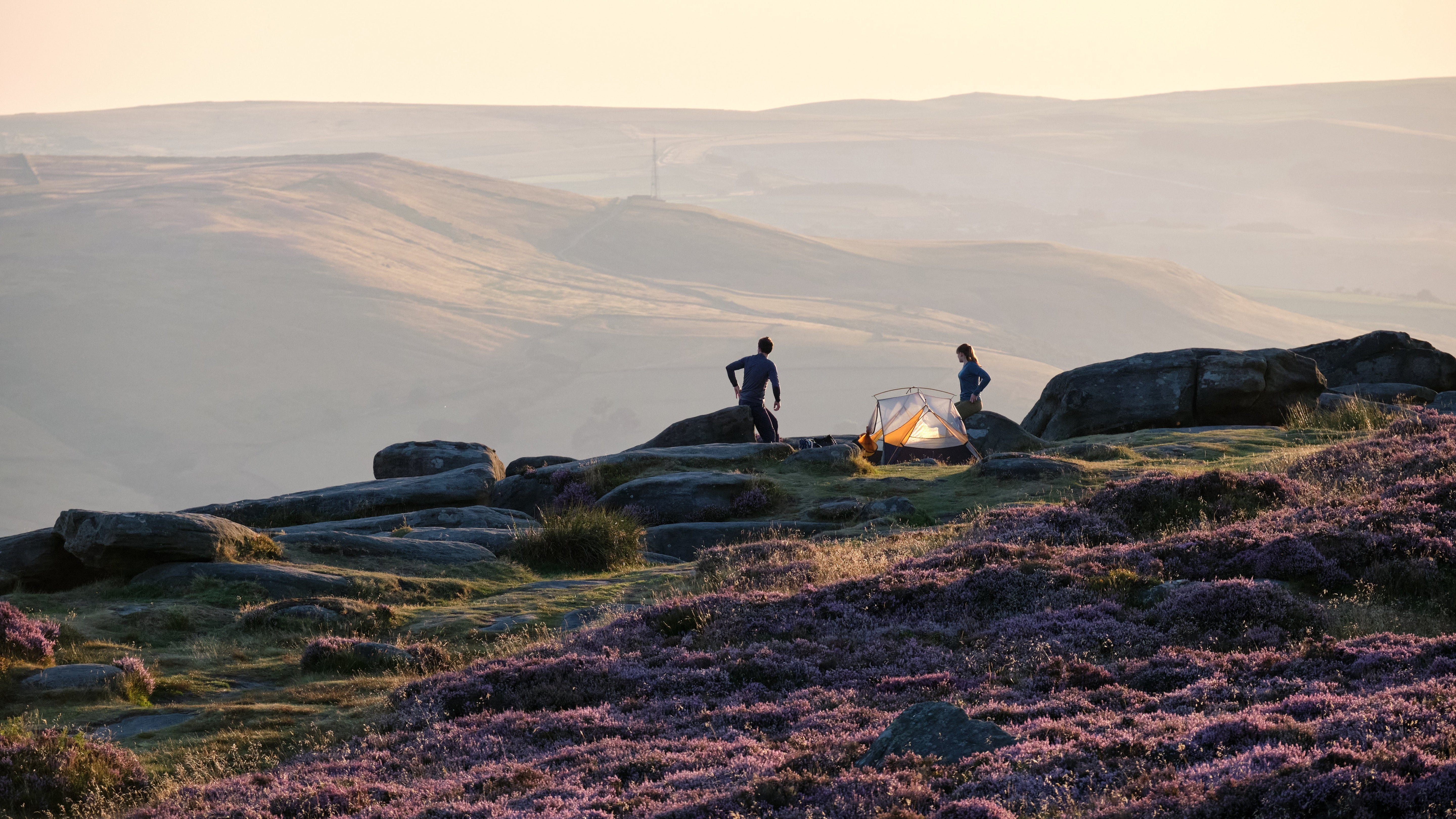 Wide shot of a tent pitched atop a hill in a valley of rolling hills