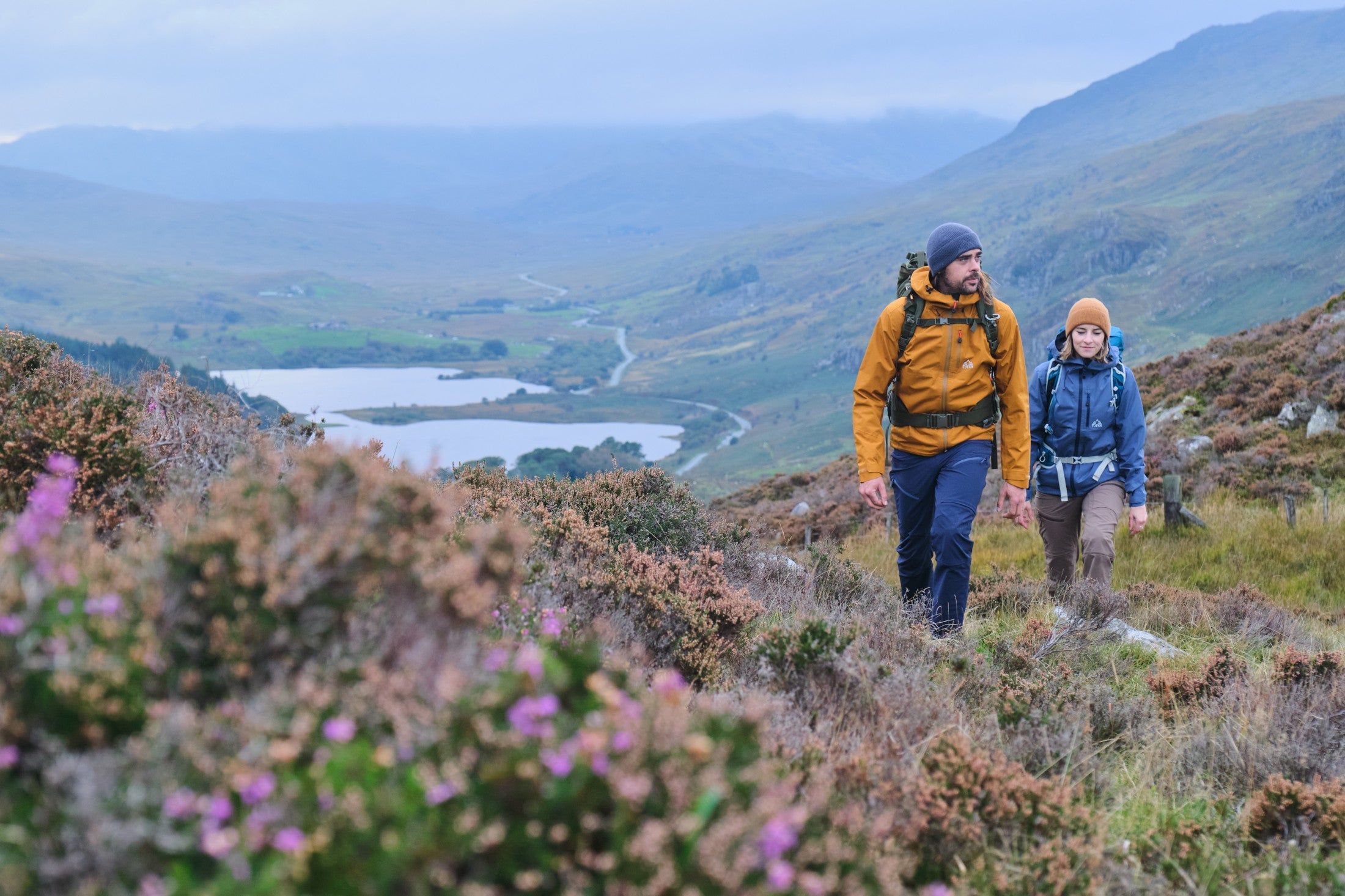 Hiking up a heather hillside above a distant lake in Forsvar Jackets