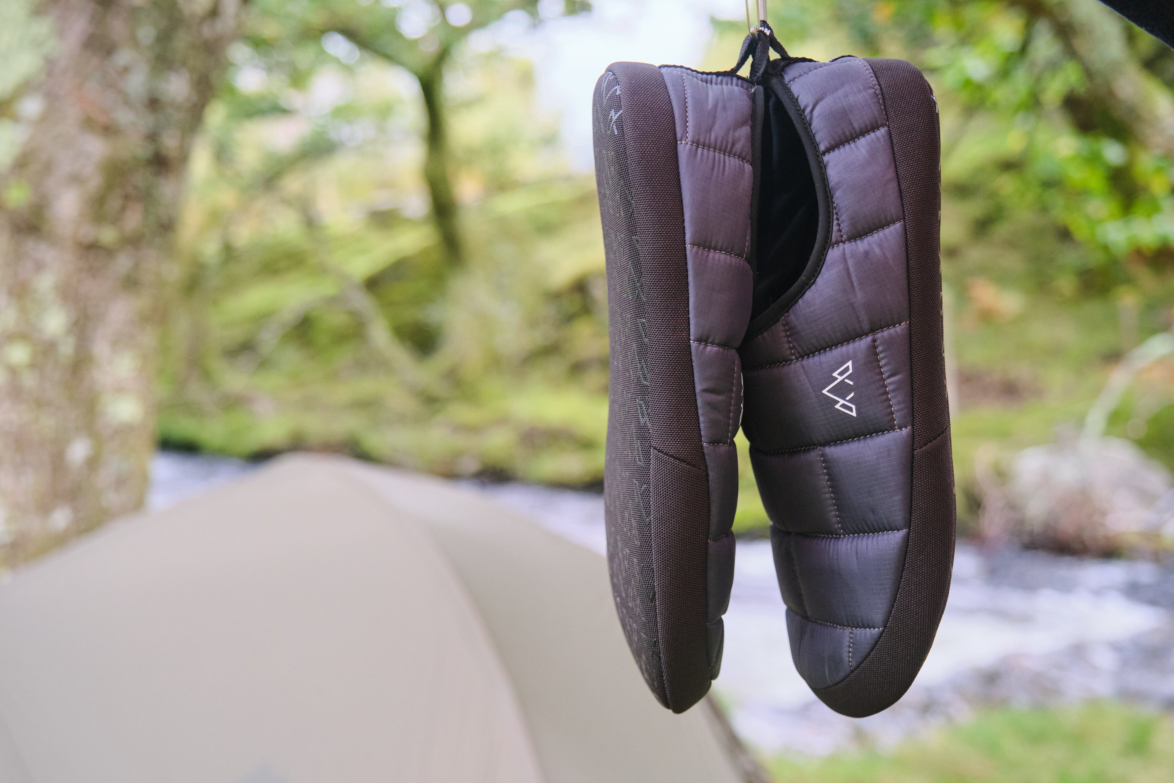 Fjern Tøffelhelt Tent Slippers hanging from a tree branch next to a tent pitched by a stream