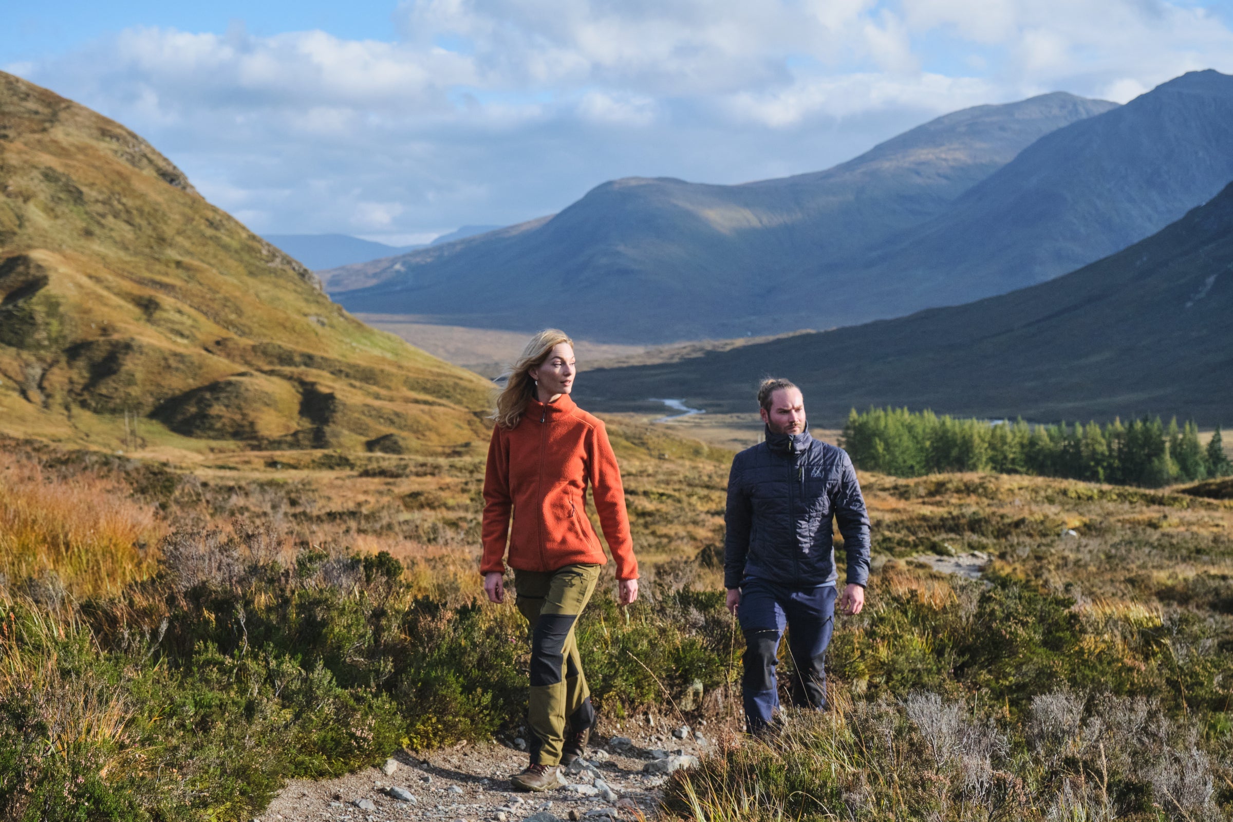 Two people walking on a trail with mountains in the background