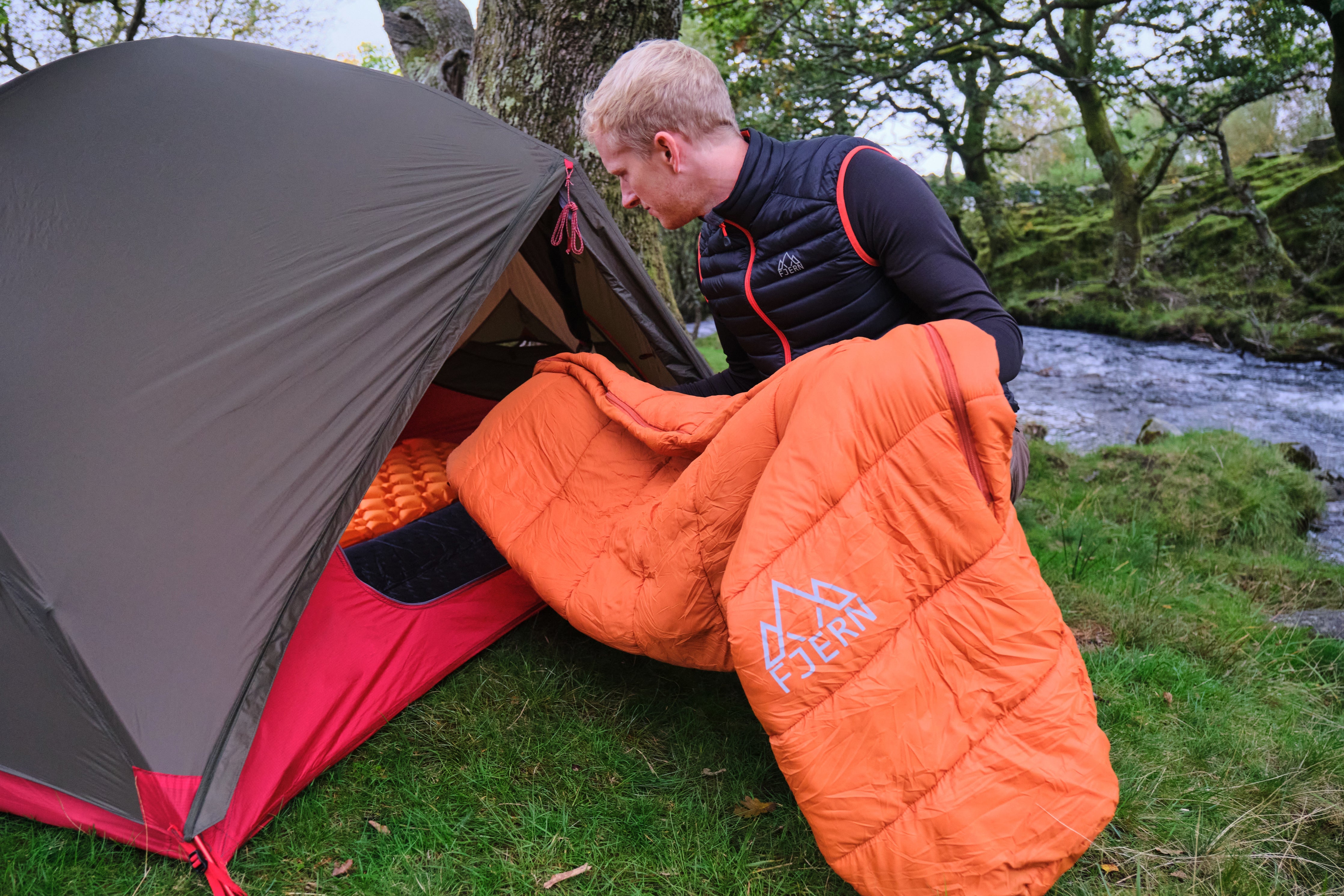 Tent pitched next to a stream featuring Fjern Snarka sleeping bag