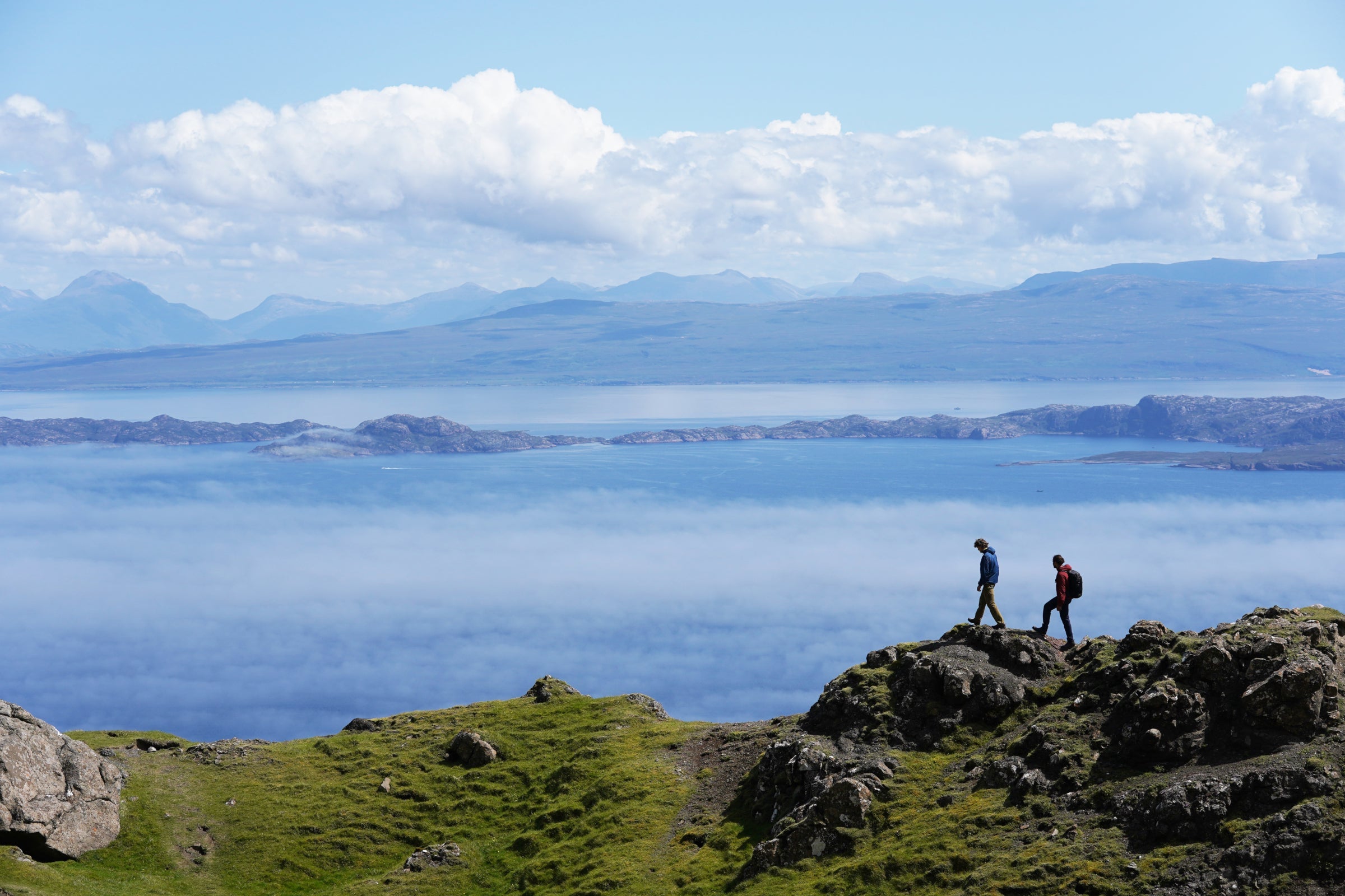 Hikers wearing Fjern gear walking along a rocky ridge with sea and mountains in the background