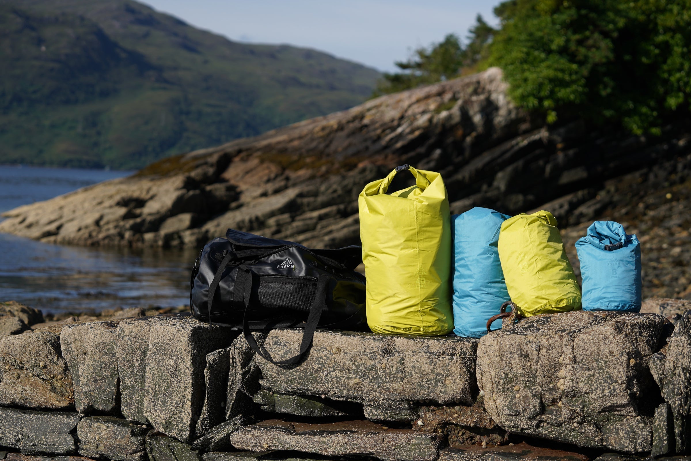 Fjern dry bags in different sizes and colours on rocks by the water