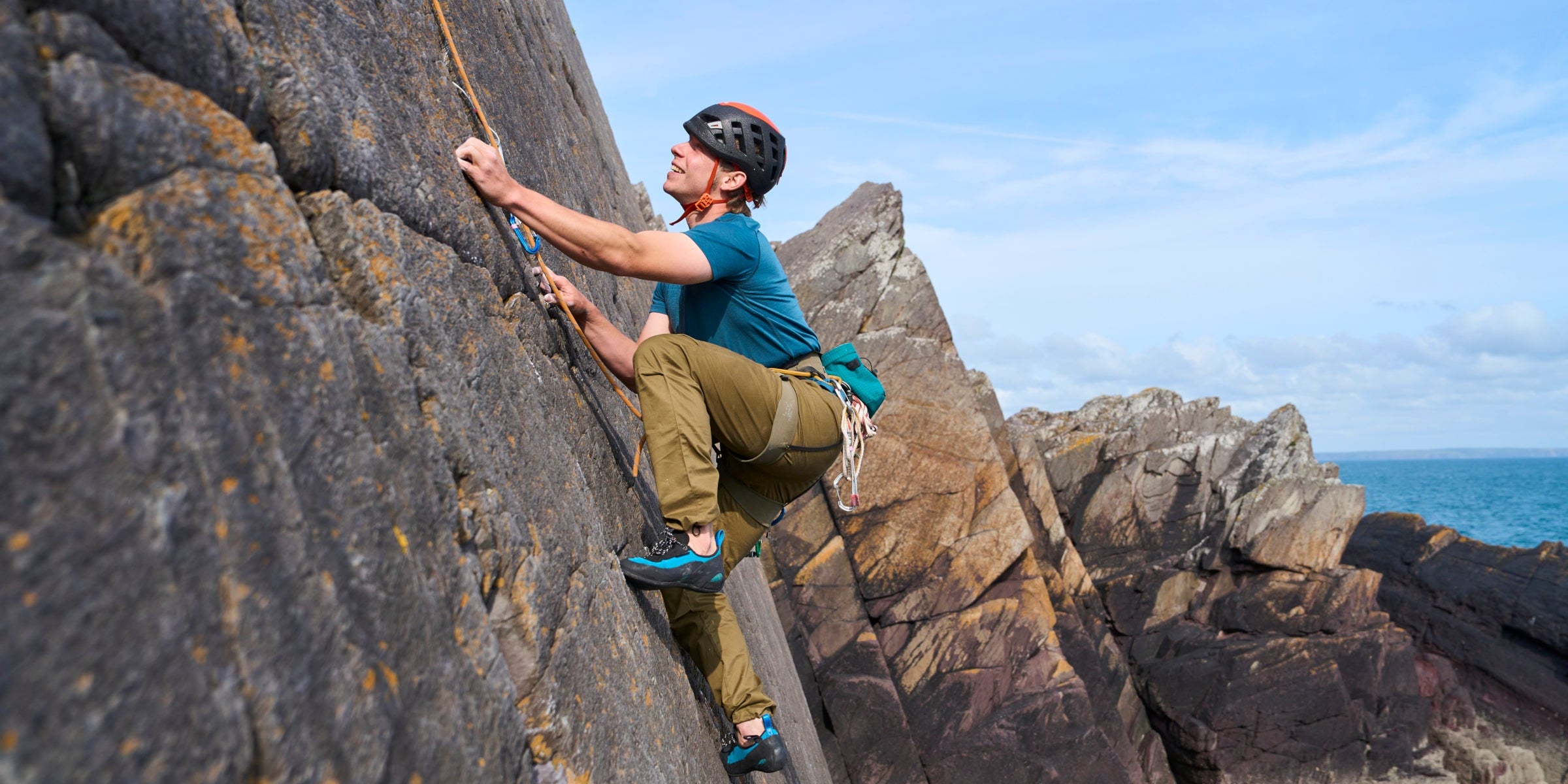 Man climbing outdoors in Fjern climbing trousers, using rope protection on a steep rock face