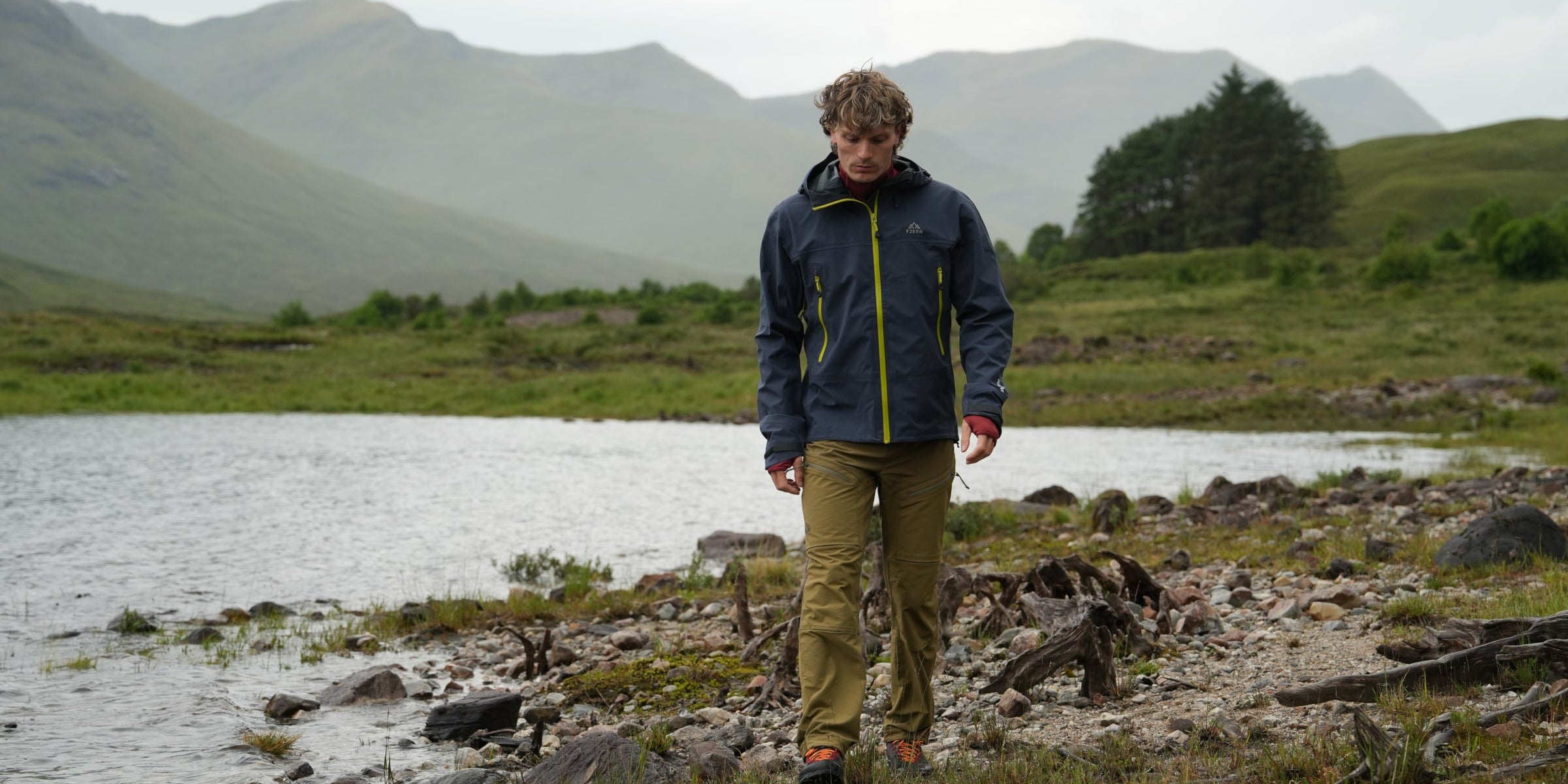 Man walking along lochside in Fjern waterproof jacket with contrasting zips