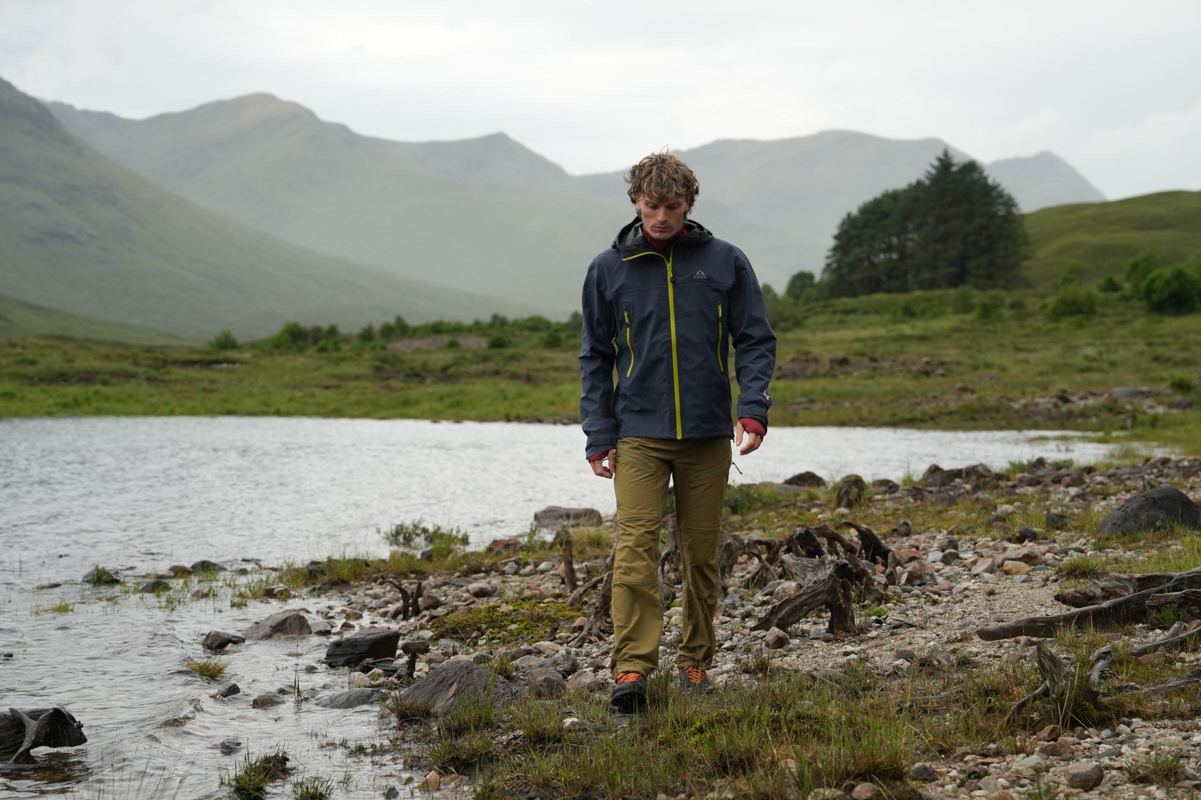 Man walking along lochside in Fjern waterproof jacket with contrasting zips