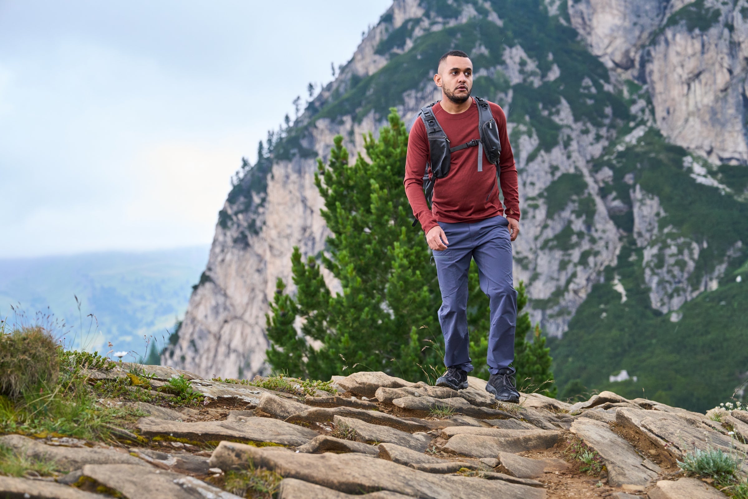 Man trekking on rocky mountain trail wearing Fjern long sleeve top with backpack