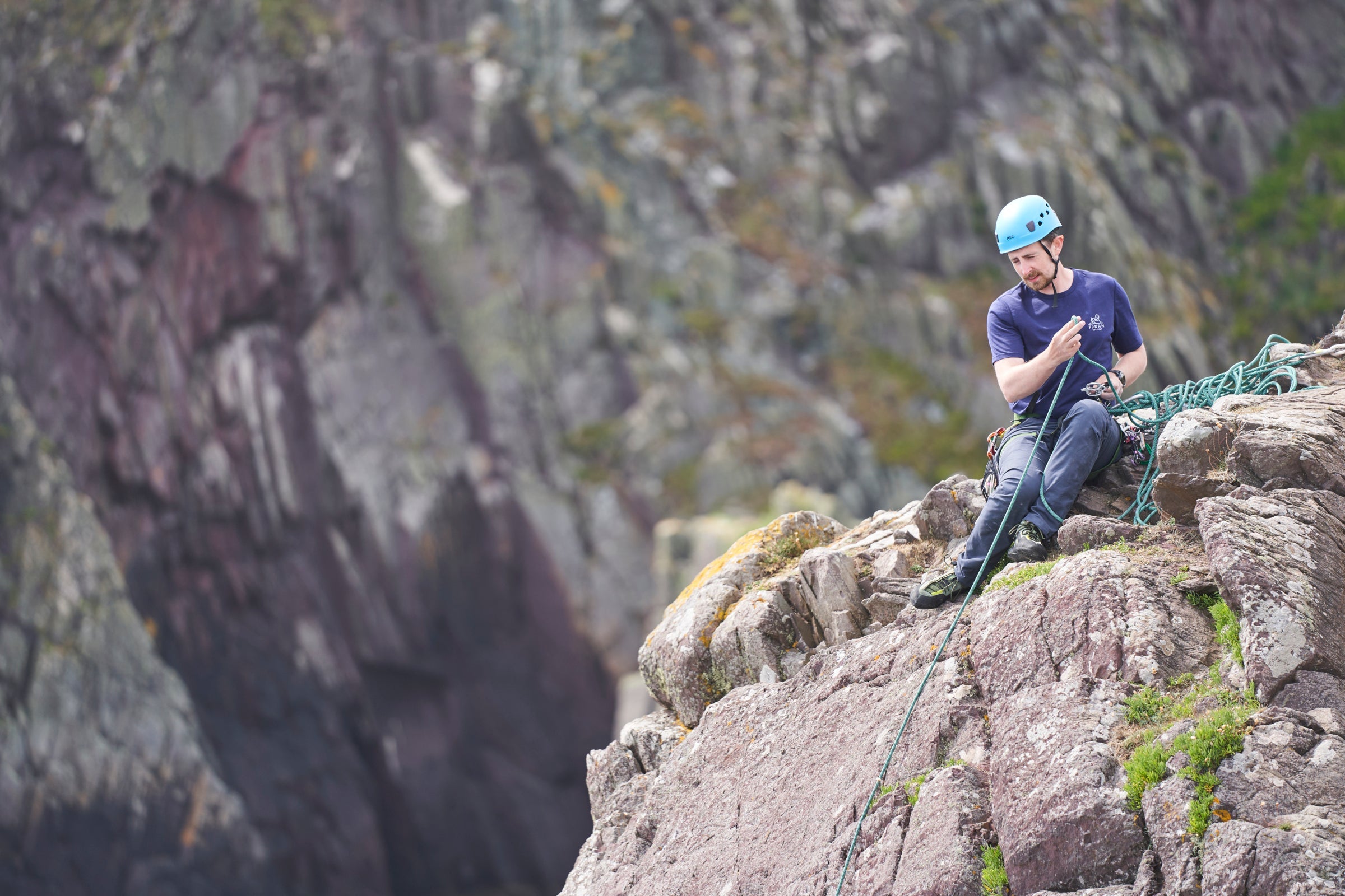 Man belaying on sea cliffs wearing Fjern short sleeve t-shirt and helmet