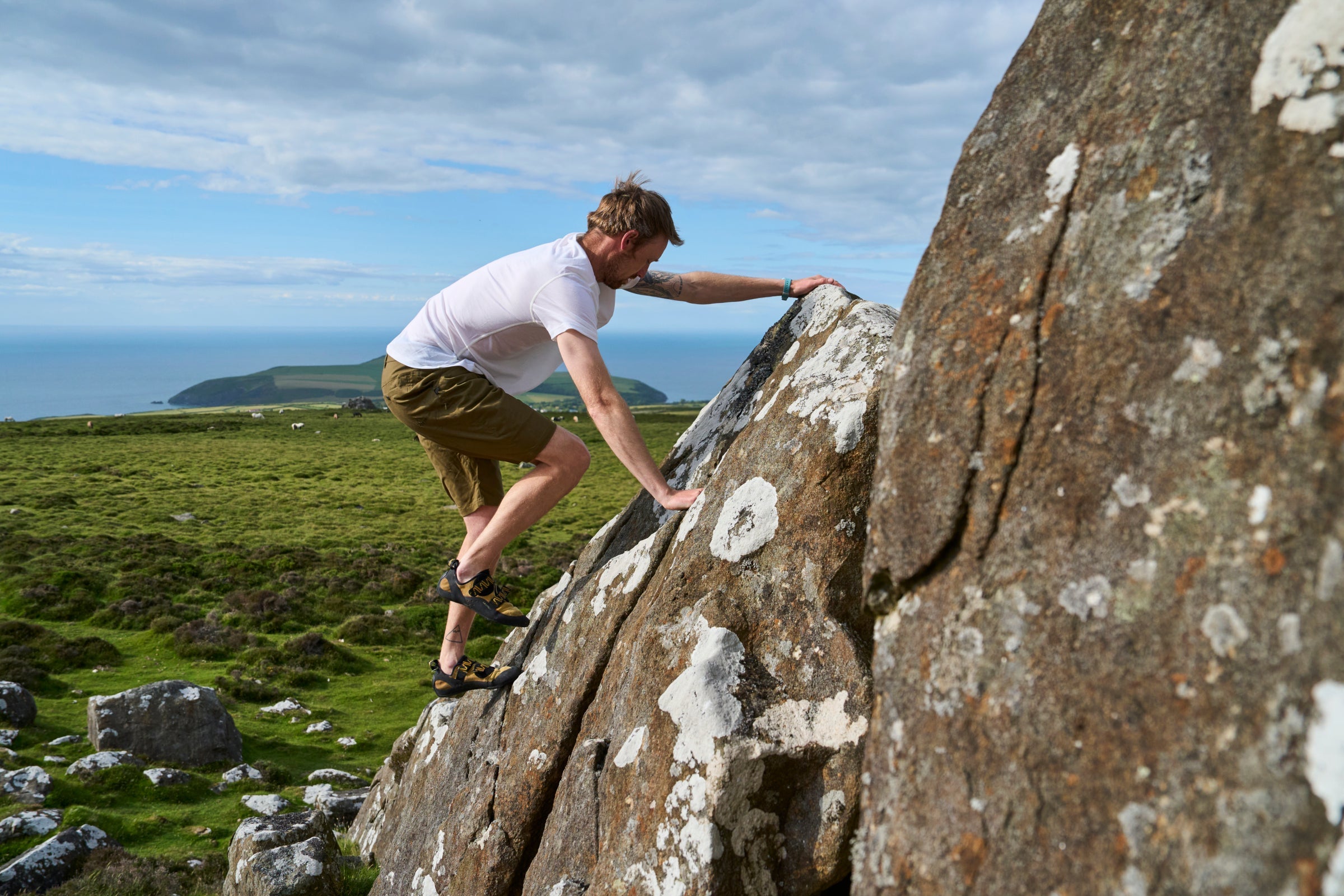 Man bouldering on rocky hillside in Fjern outdoor shorts with sea views in the distance