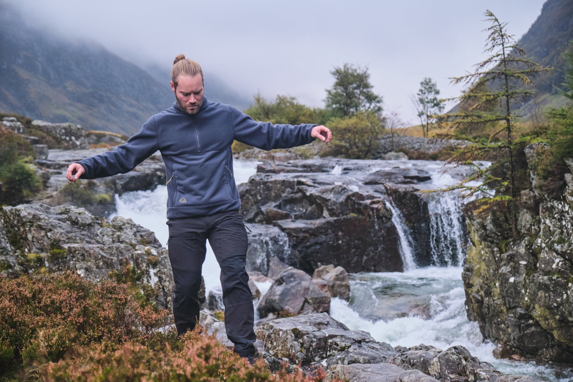 Man walking near waterfall in Fjern softshell trousers and fleece