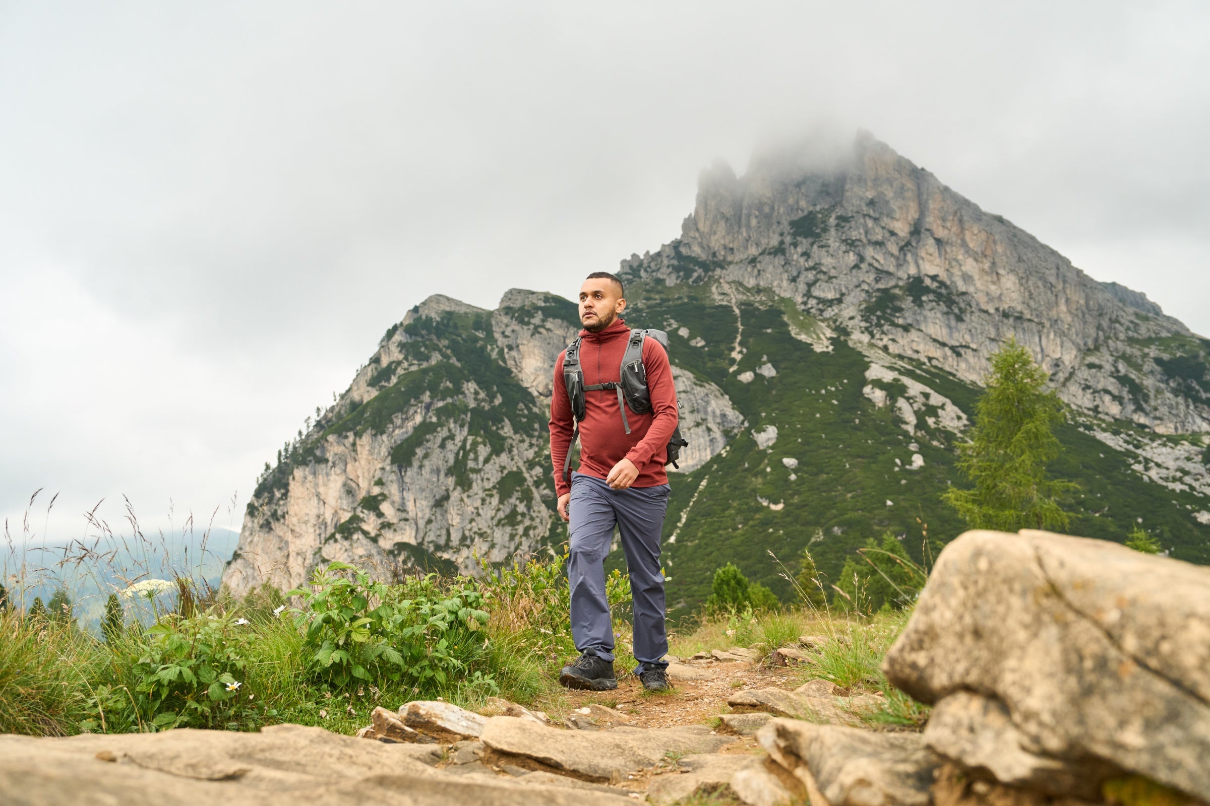 Man hiking on rocky mountain trail wearing Fjern long sleeve performance top.