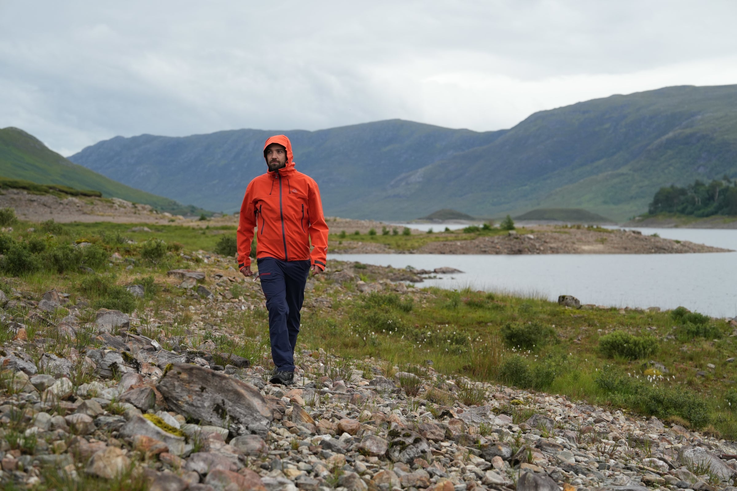 Man hiking by a rocky riverside wearing Fjern waterproof jacket with hood