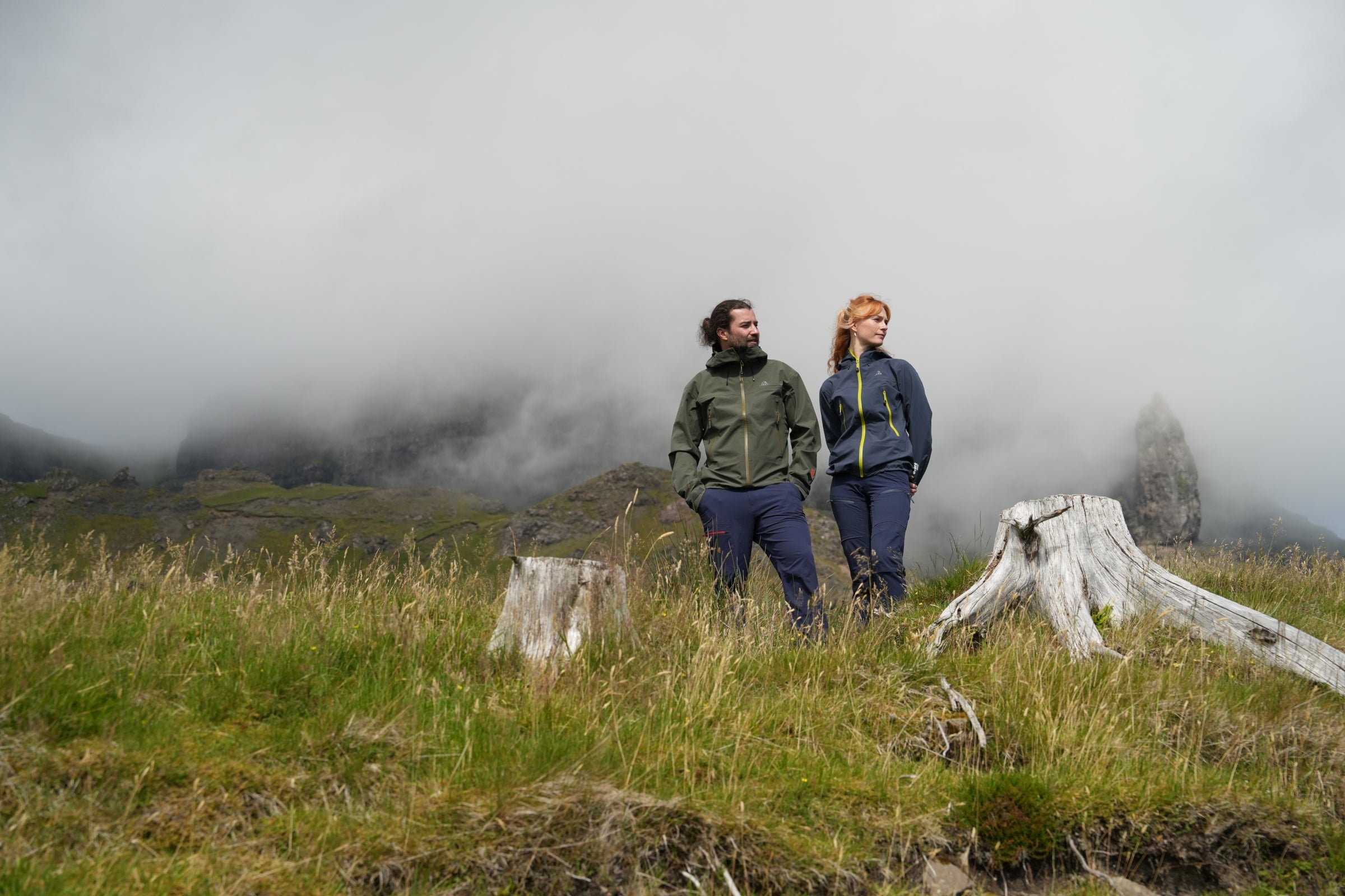 Two people wearing Orkan II jackets standing outdoors in a misty mountain landscape