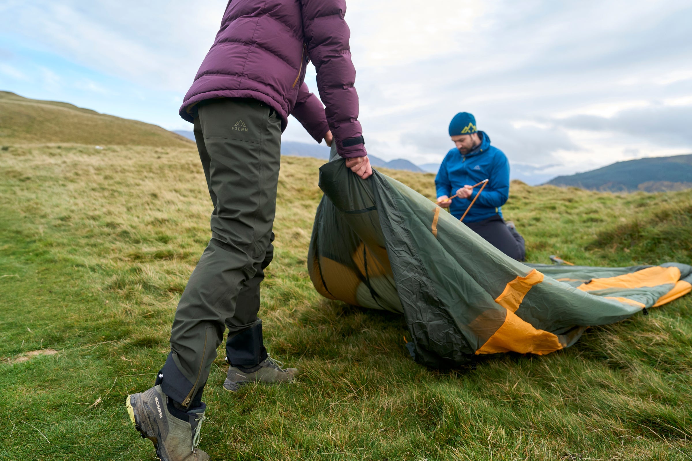 Person wearing Vernd WP trousers pitching a tent outdoors