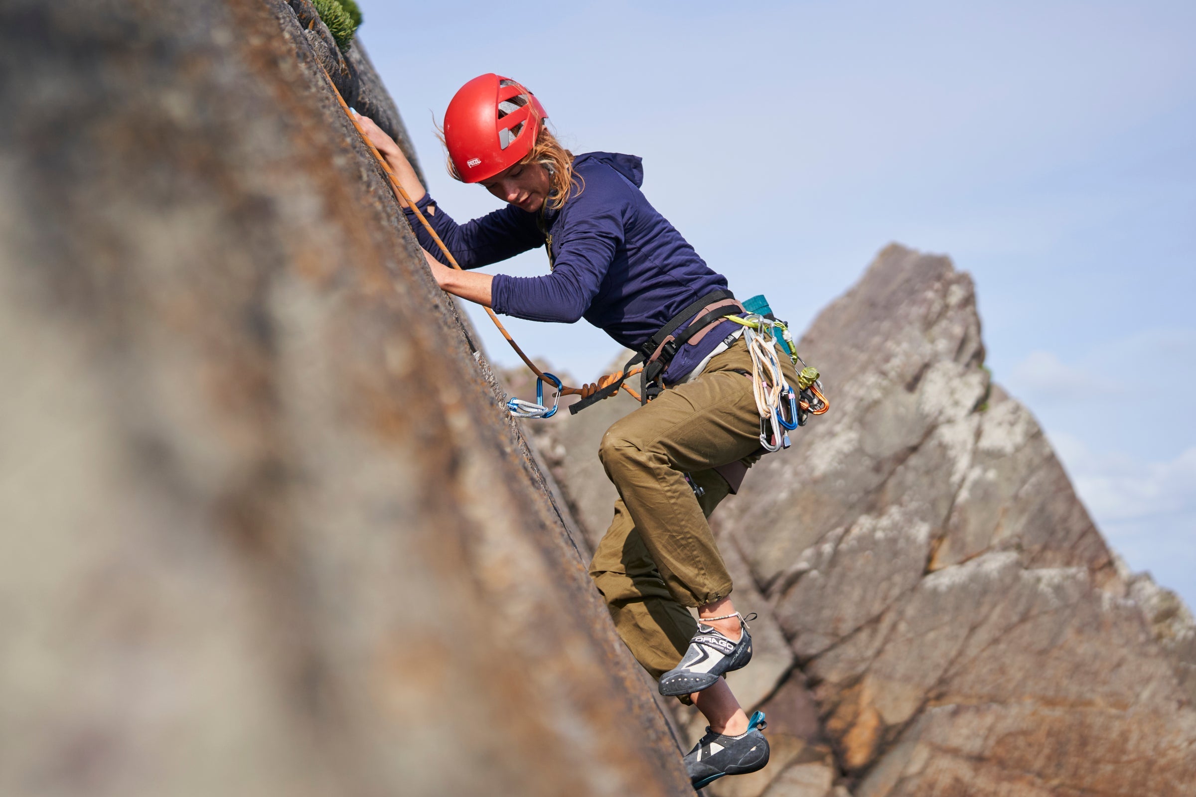Woman climbing outdoors in Fjern climbing trousers, secured with harness and rope on coastal rock