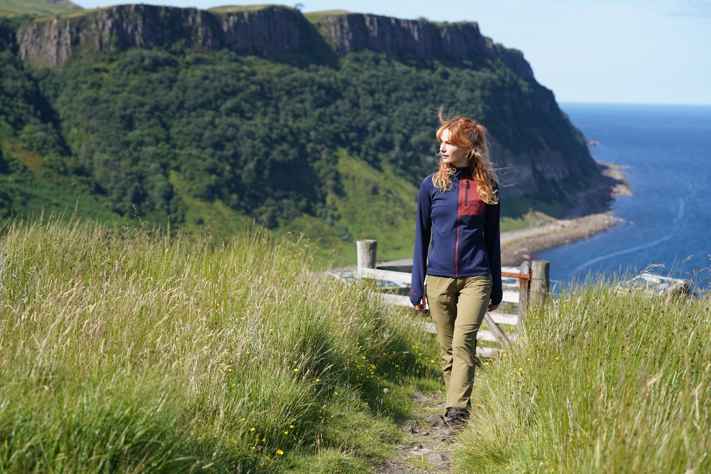 Woman hiking coastal trail in Fjern fleece jacket, with sea cliffs in the background