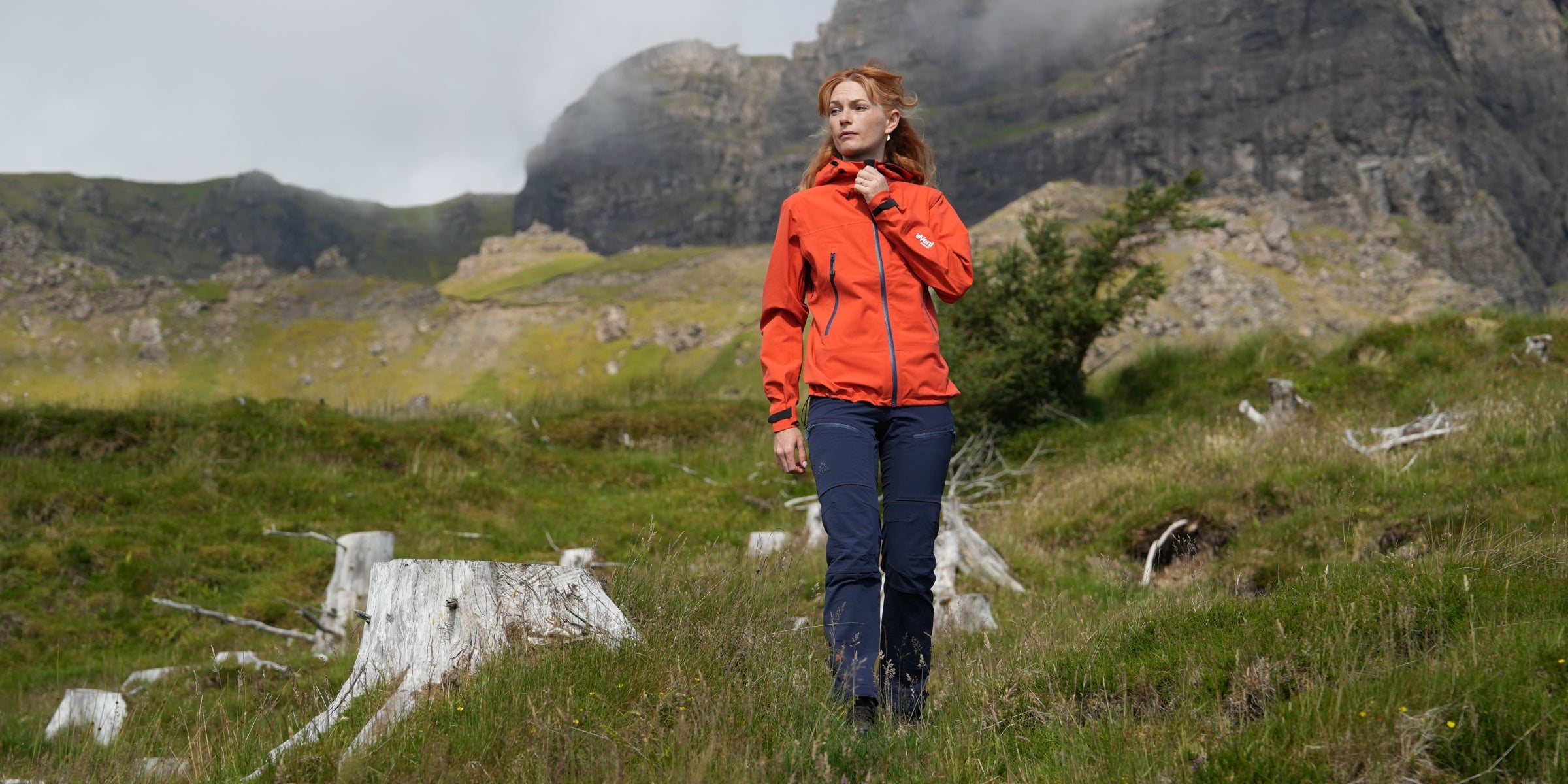Woman walking in the mountains wearing Fjern outdoor jacket, adjusting collar