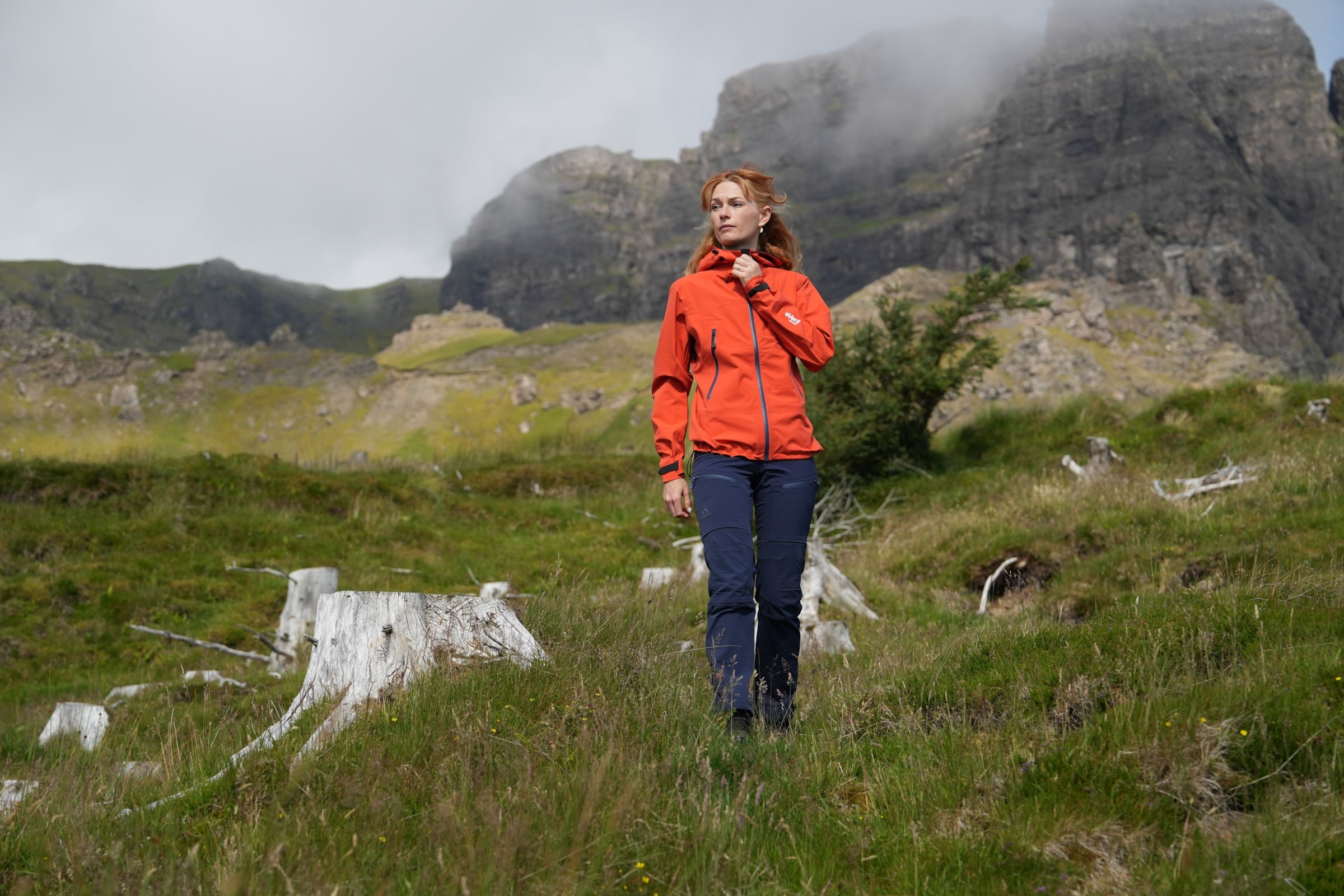 Woman walking in the mountains wearing Fjern outdoor jacket, adjusting collar