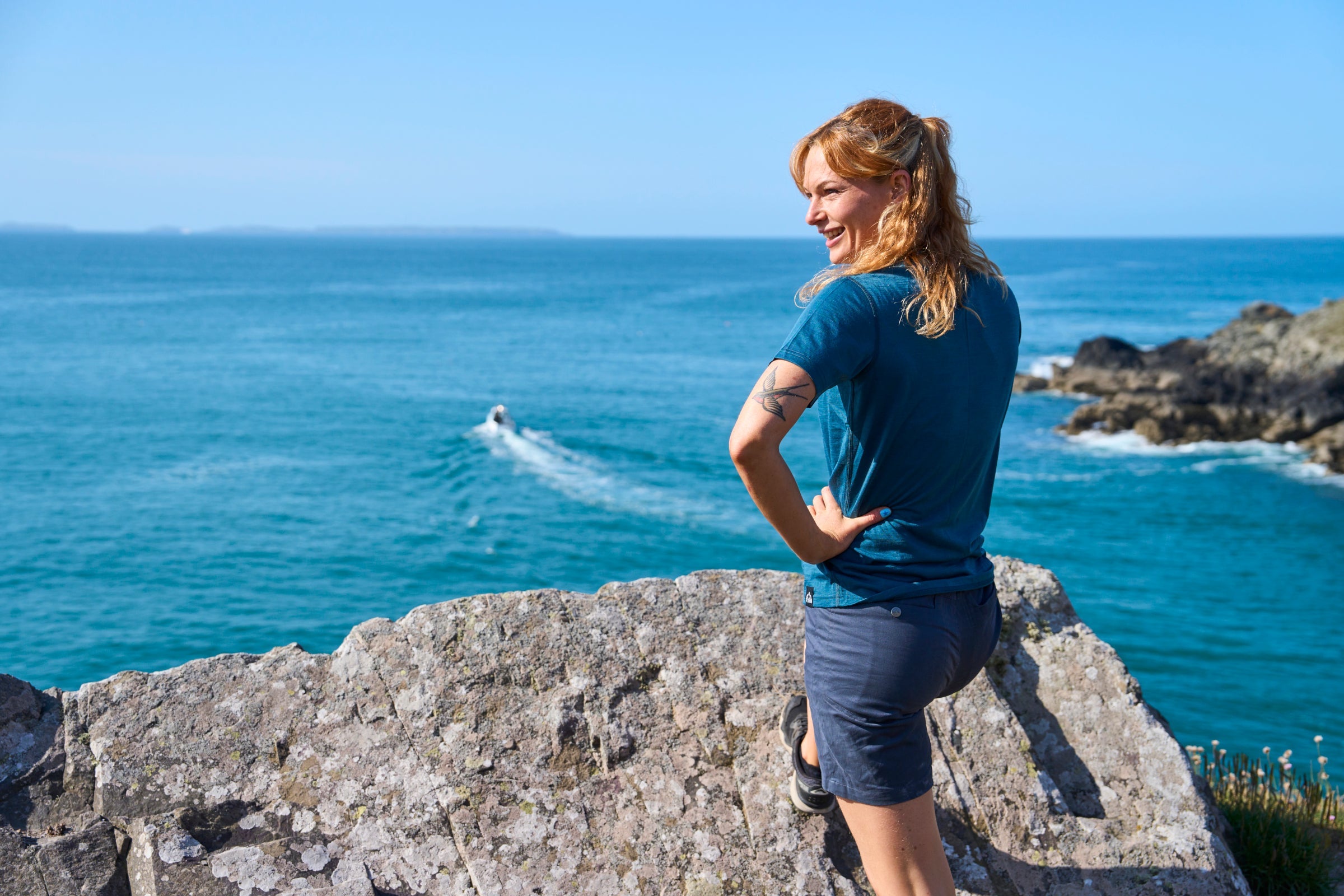 Woman standing on coastal rocks in Fjern hiking shorts, overlooking the sea