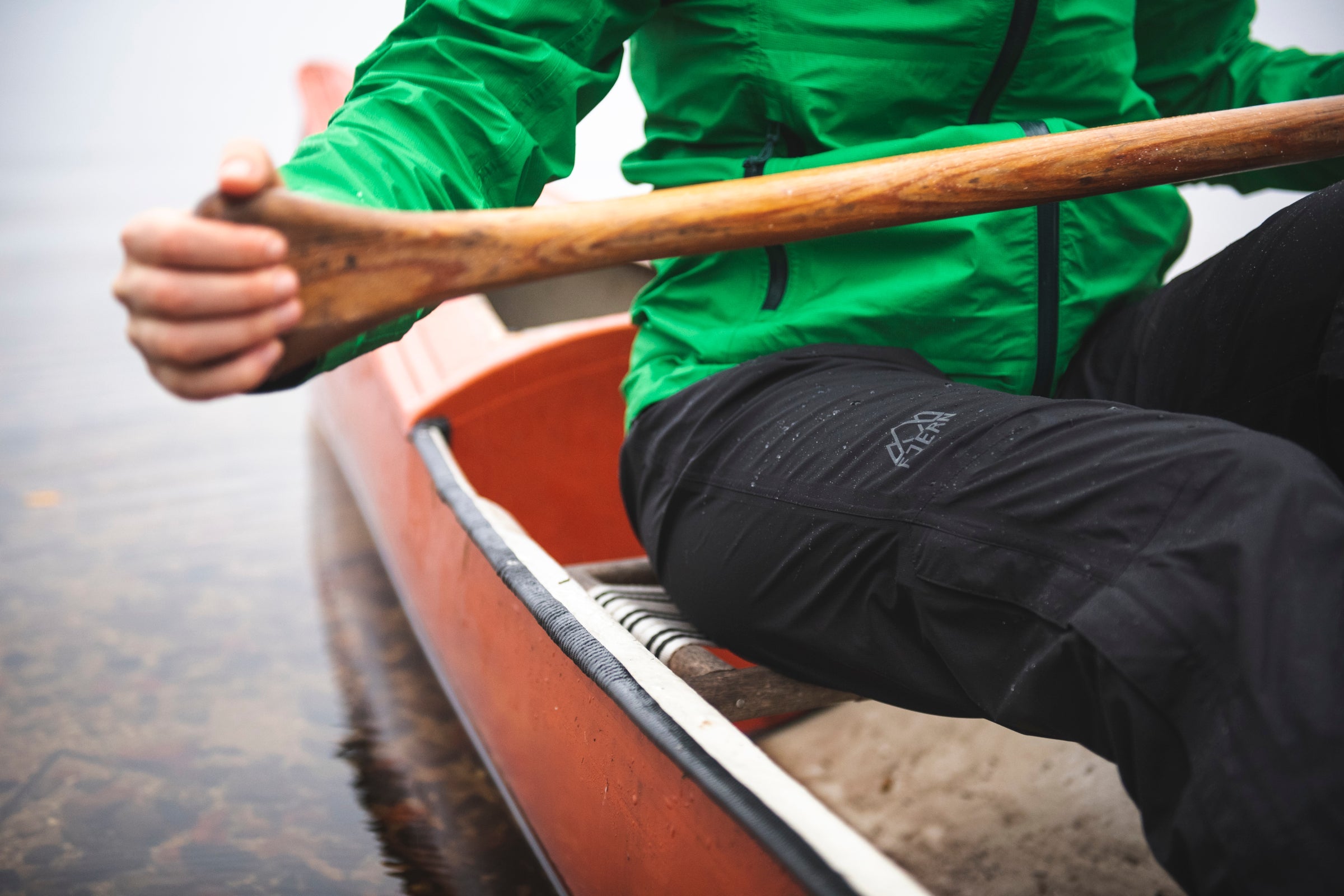 Close-up of woman paddling canoe wearing Fjern waterproof trousers