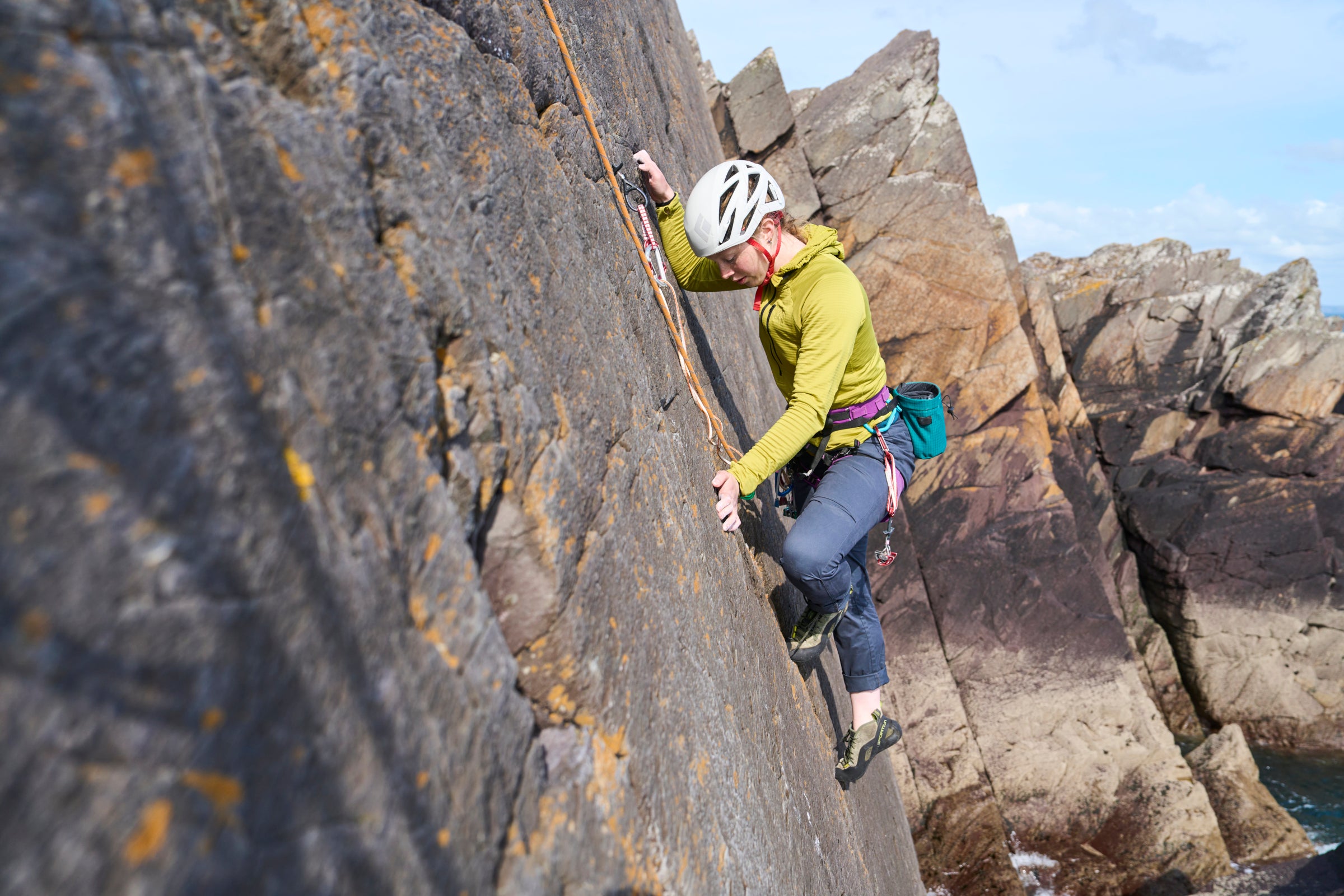 Person rock climbing on a rocky cliff face with a helmet and climbing gear
