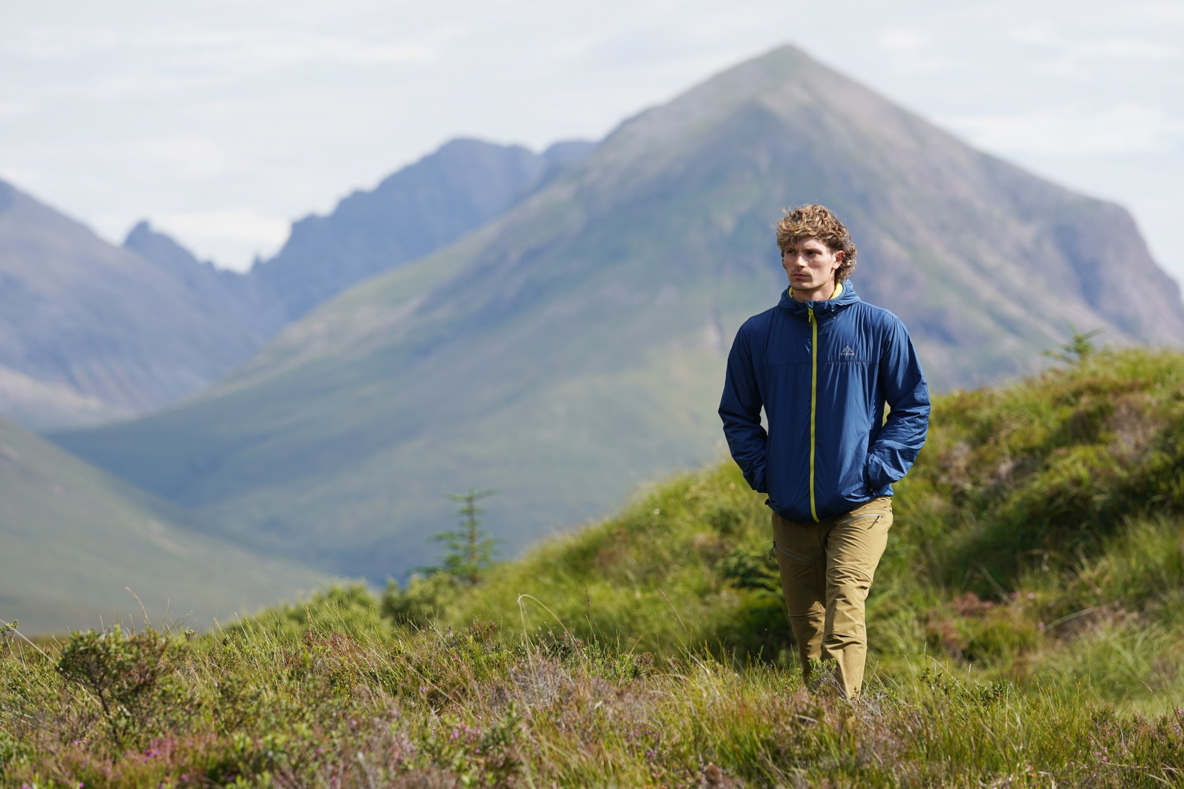 Man walking on a mountain hillside in a blue jacket