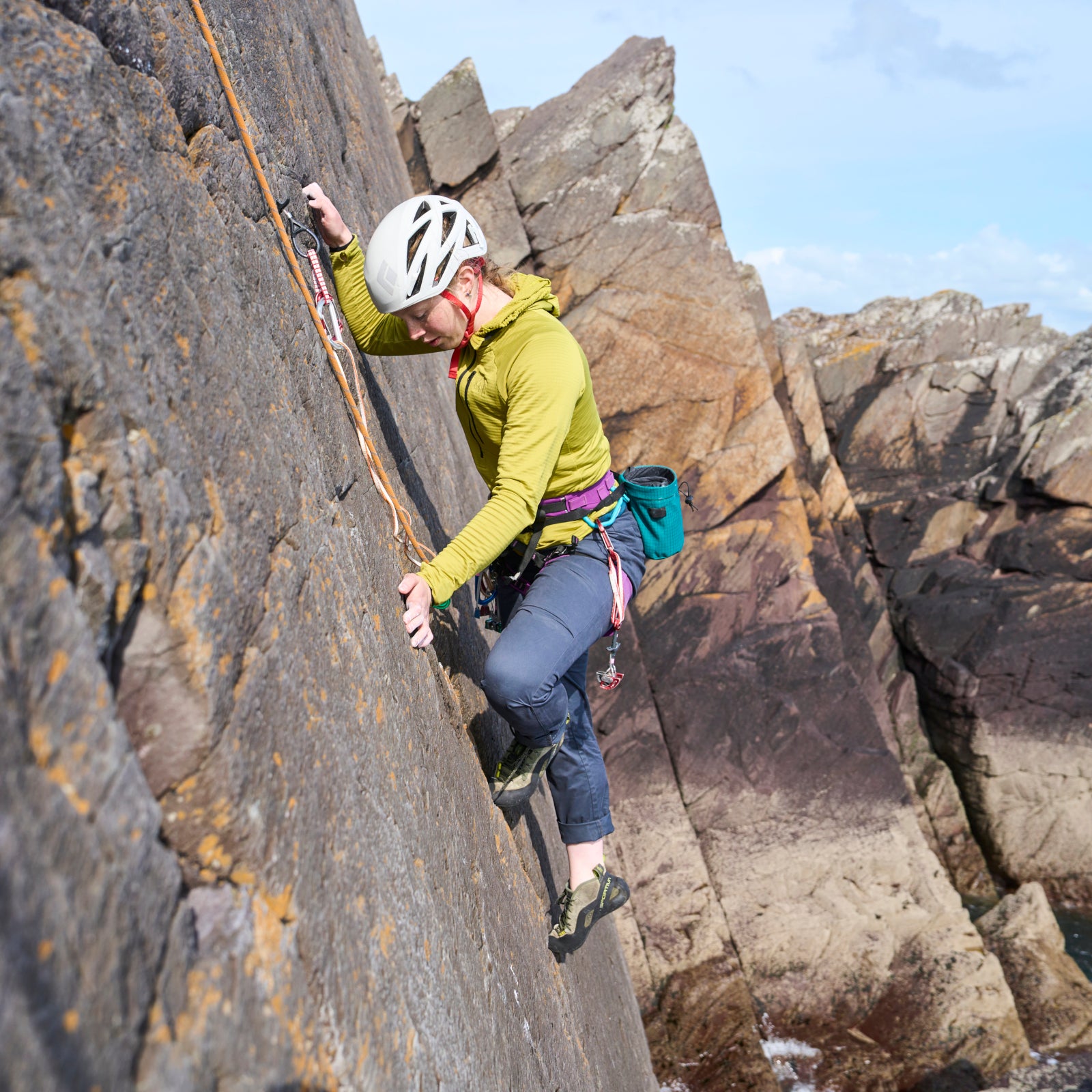 Person rock climbing on a rocky cliff face with a helmet and climbing gear