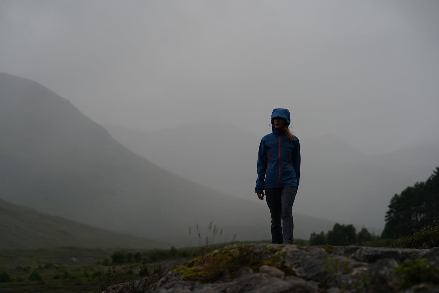 Person wearing a waterproof jacket walking through misty mountains