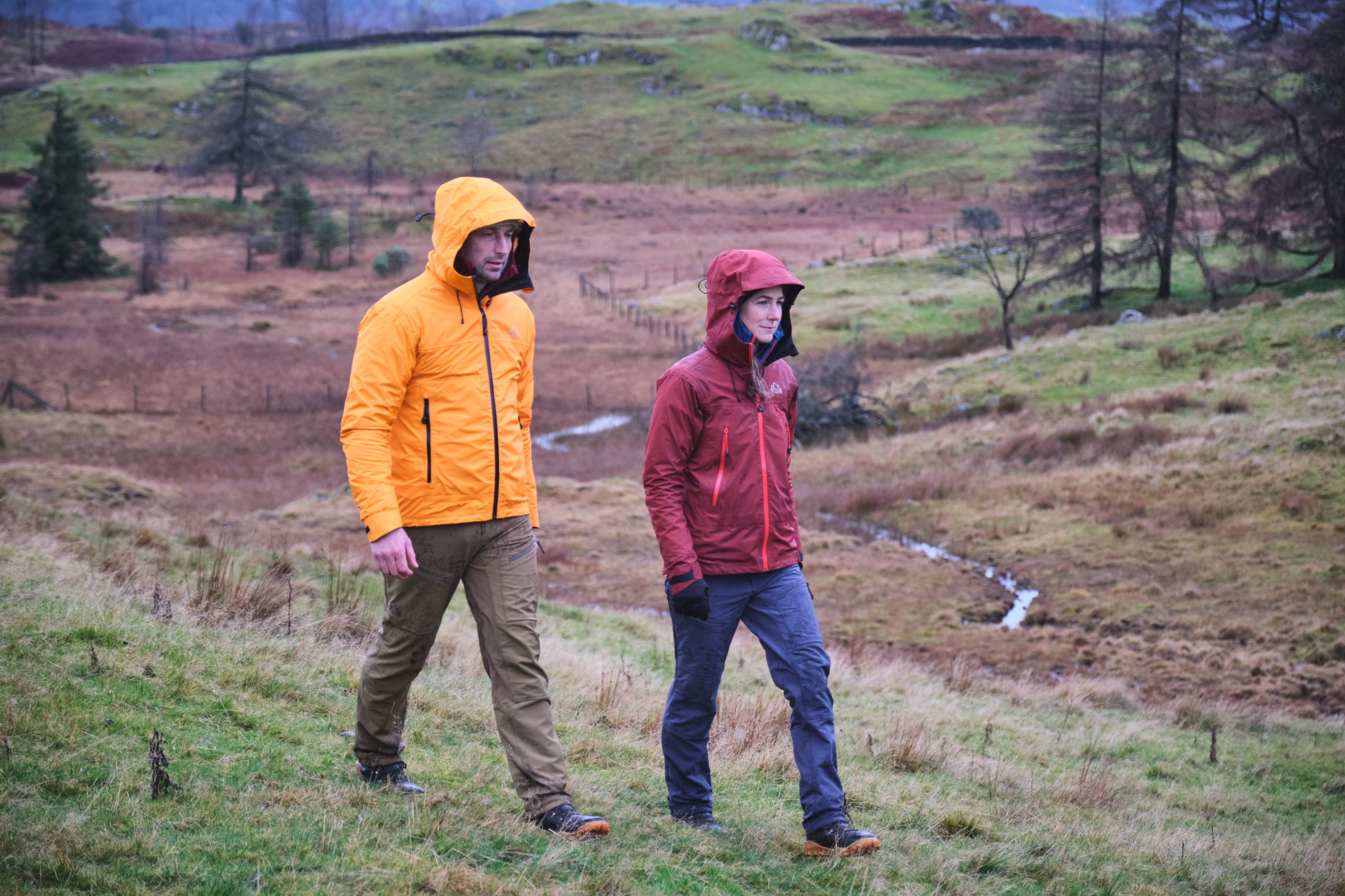 Two people hiking through a grassy field with hills in the background