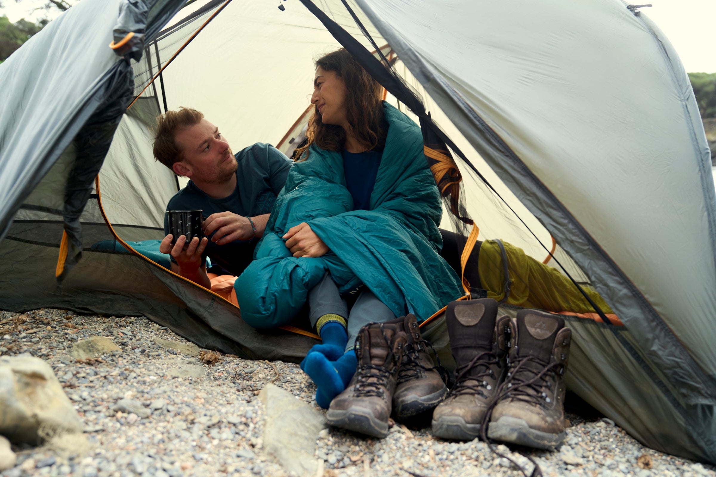 Two people sitting inside a tent with camping gear around them