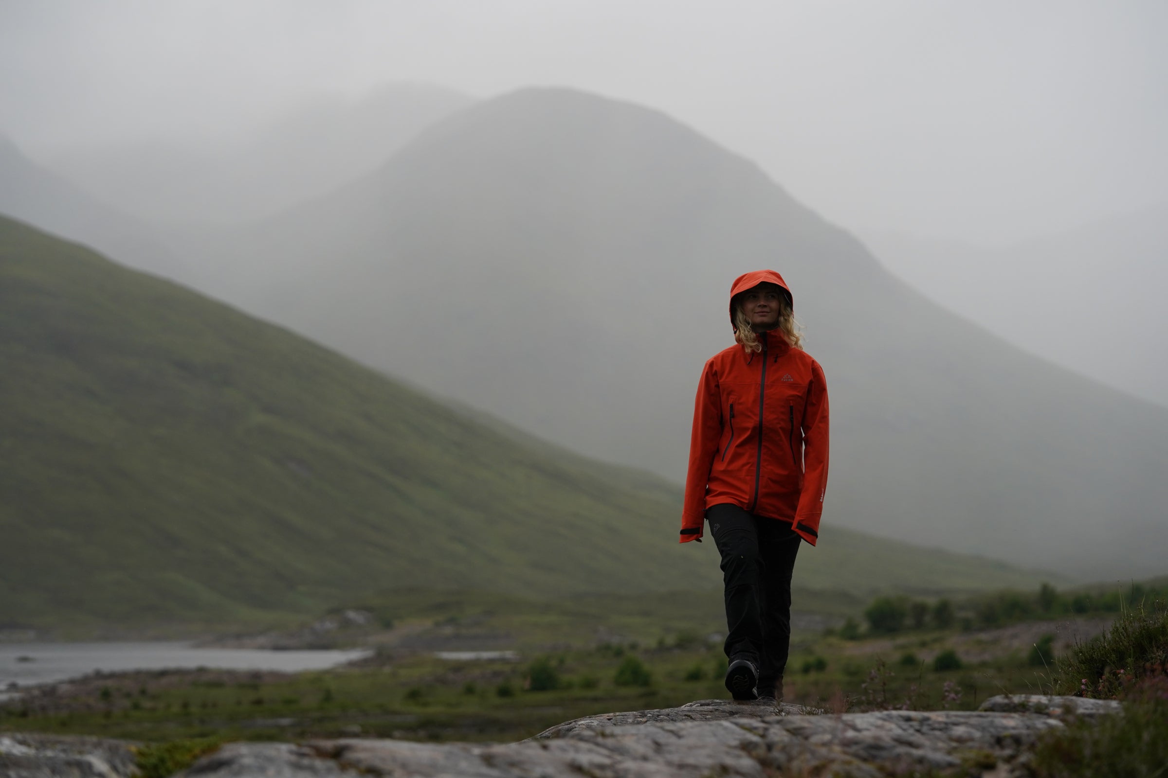 Woman hiking in misty mountains wearing Fjern waterproof jacket with hood up